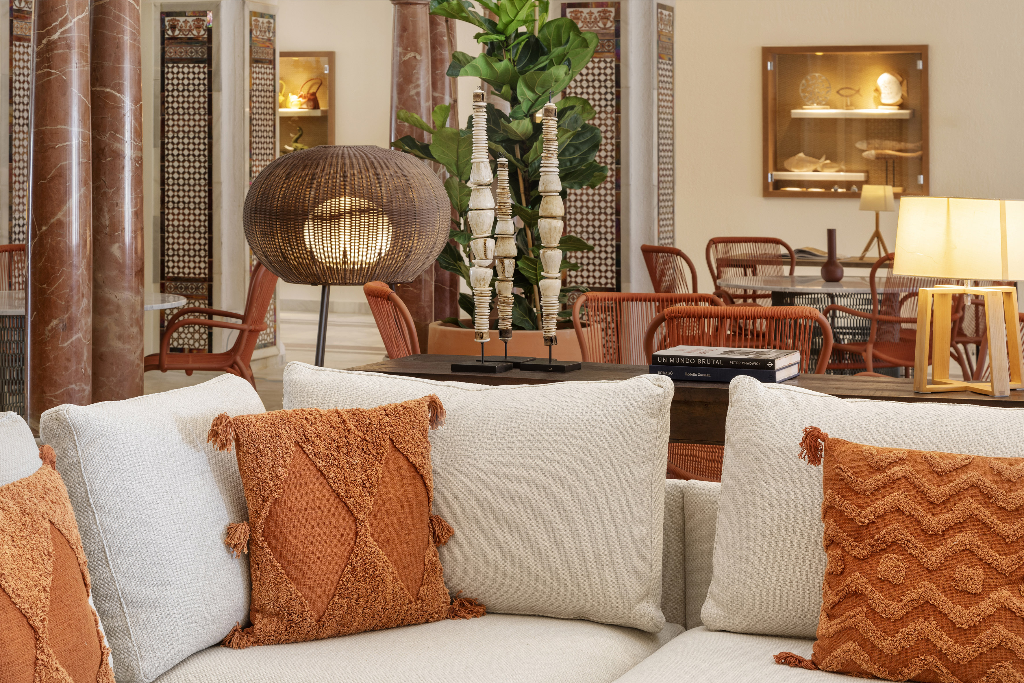Elegant hotel lobby with white sofa, orange accent pillows, and warm rattan lamp.