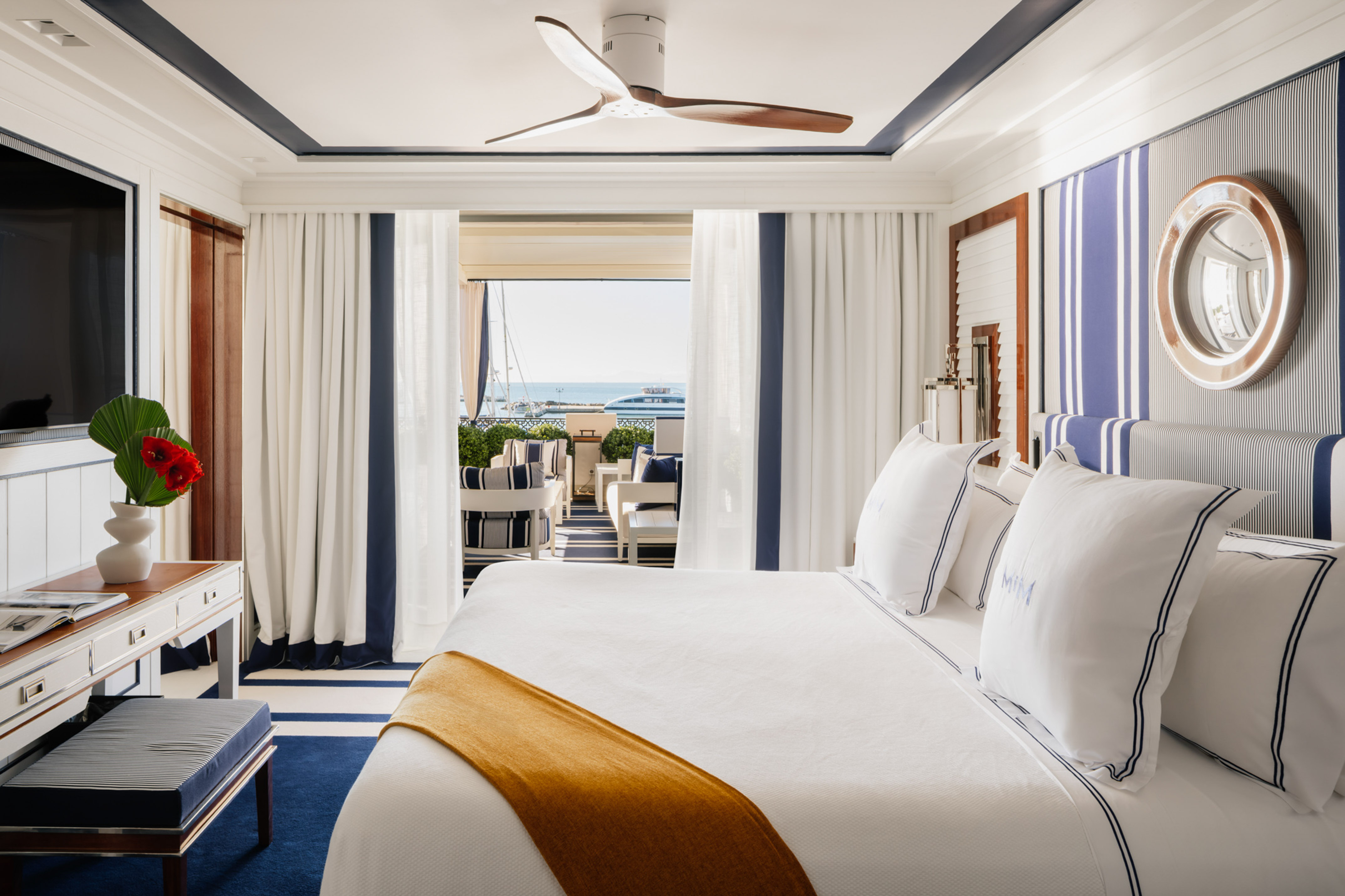 Luxury nautical bedroom with sea view balcony, white and blue decor, and marina boats.