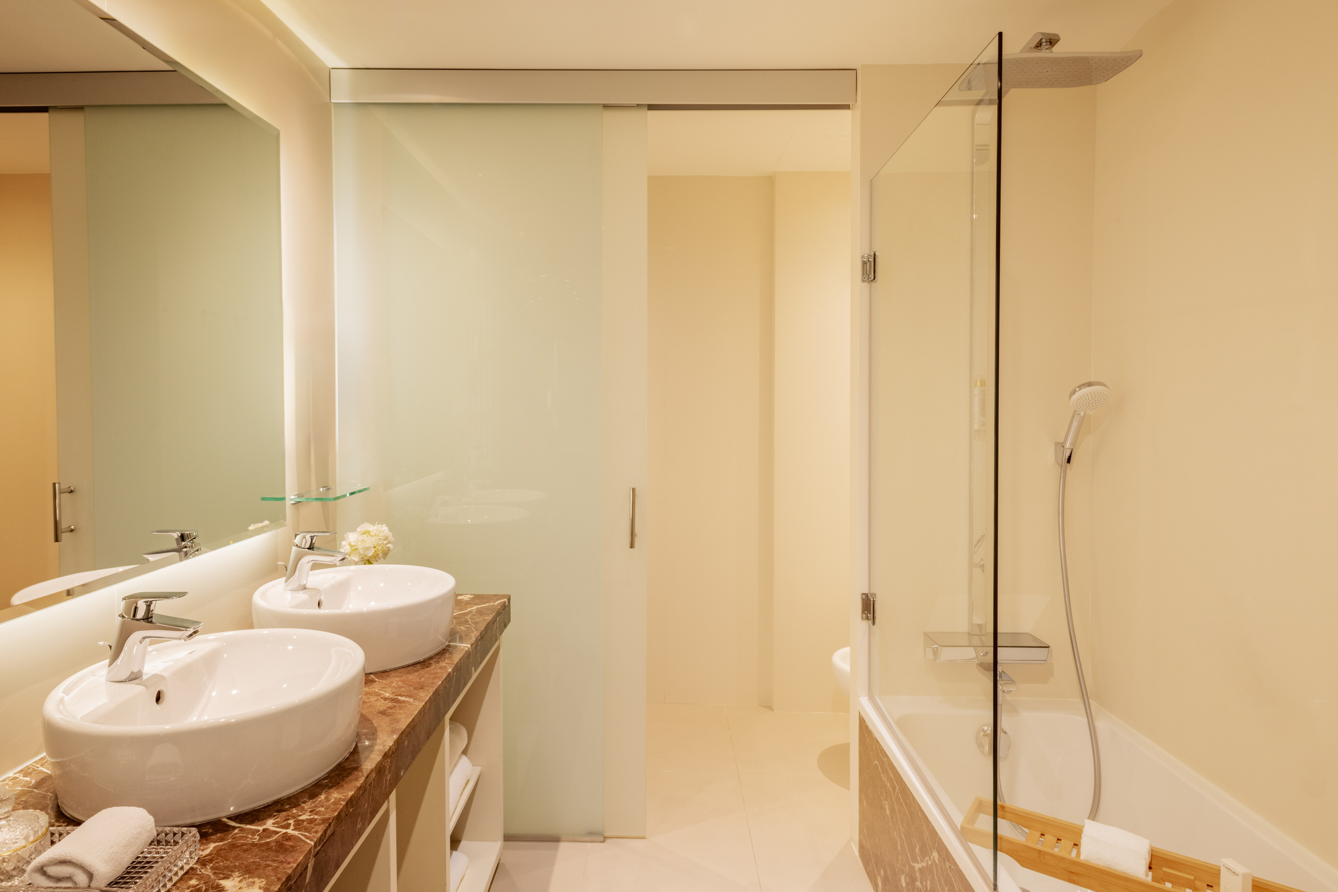 Modern hotel bathroom with dual sinks, marble counter, bathtub, and glass shower.