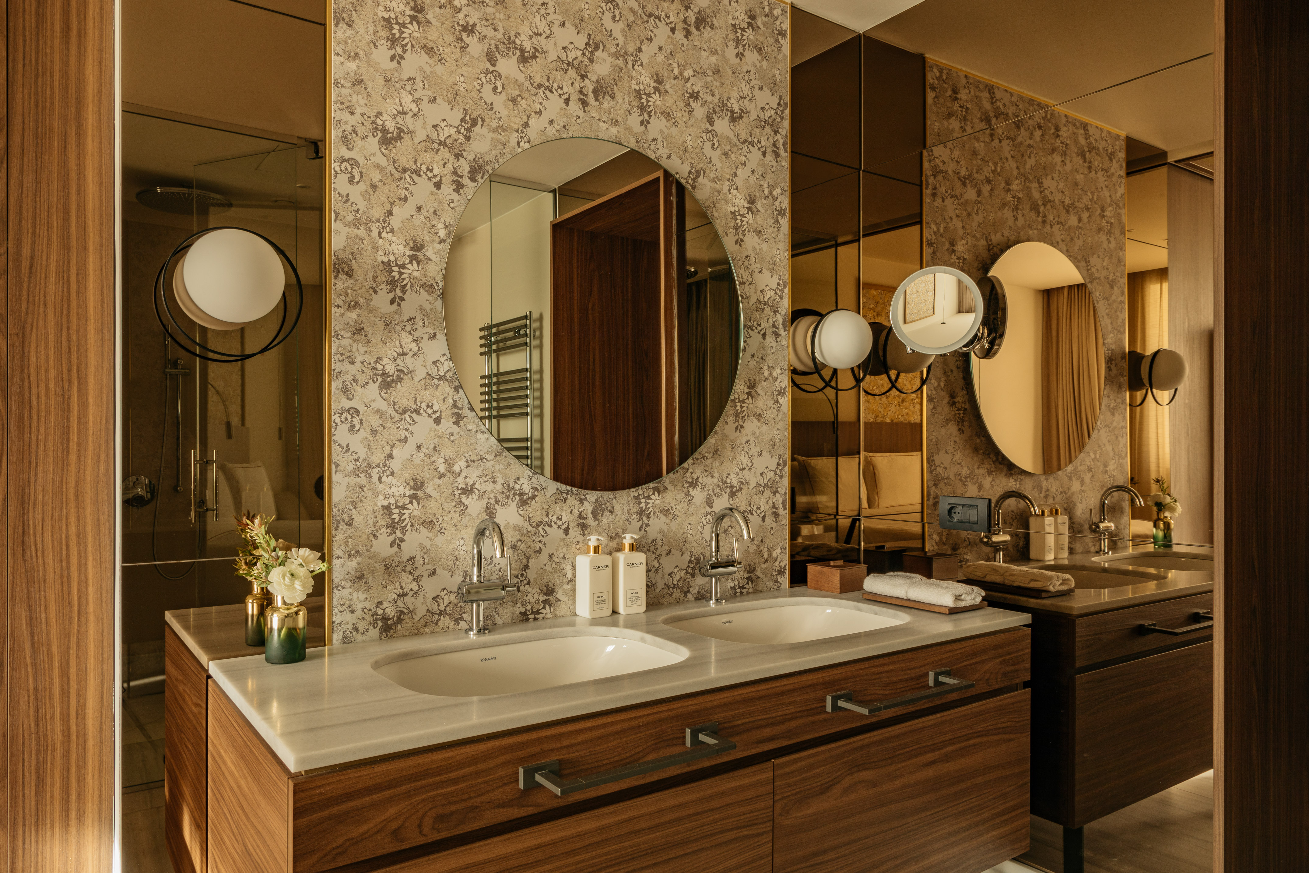 Modern bathroom with double vanity, dark wood, marble counter, and patterned wall.