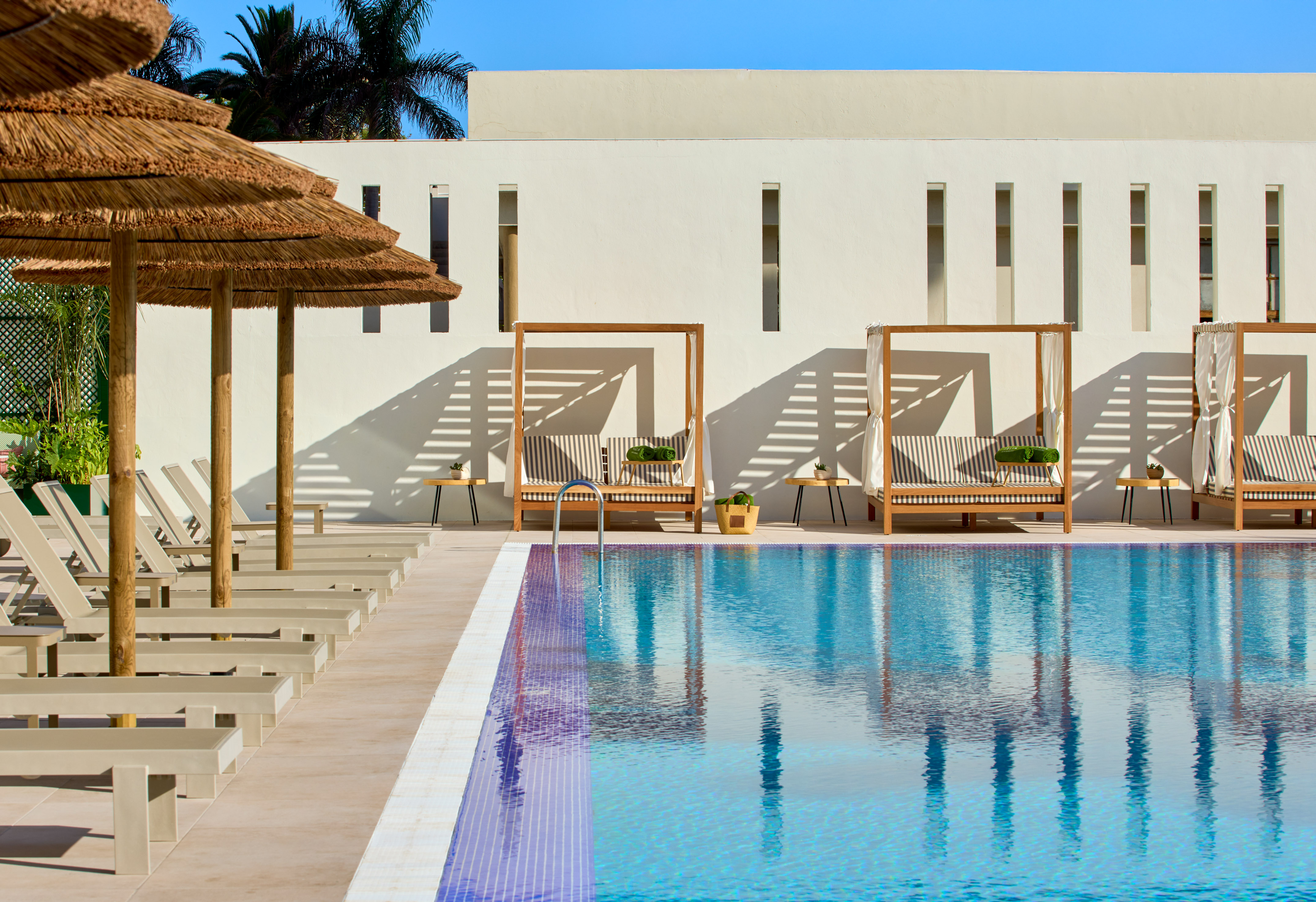 Modern resort pool with thatched umbrellas, sunbeds, and cabana loungers.