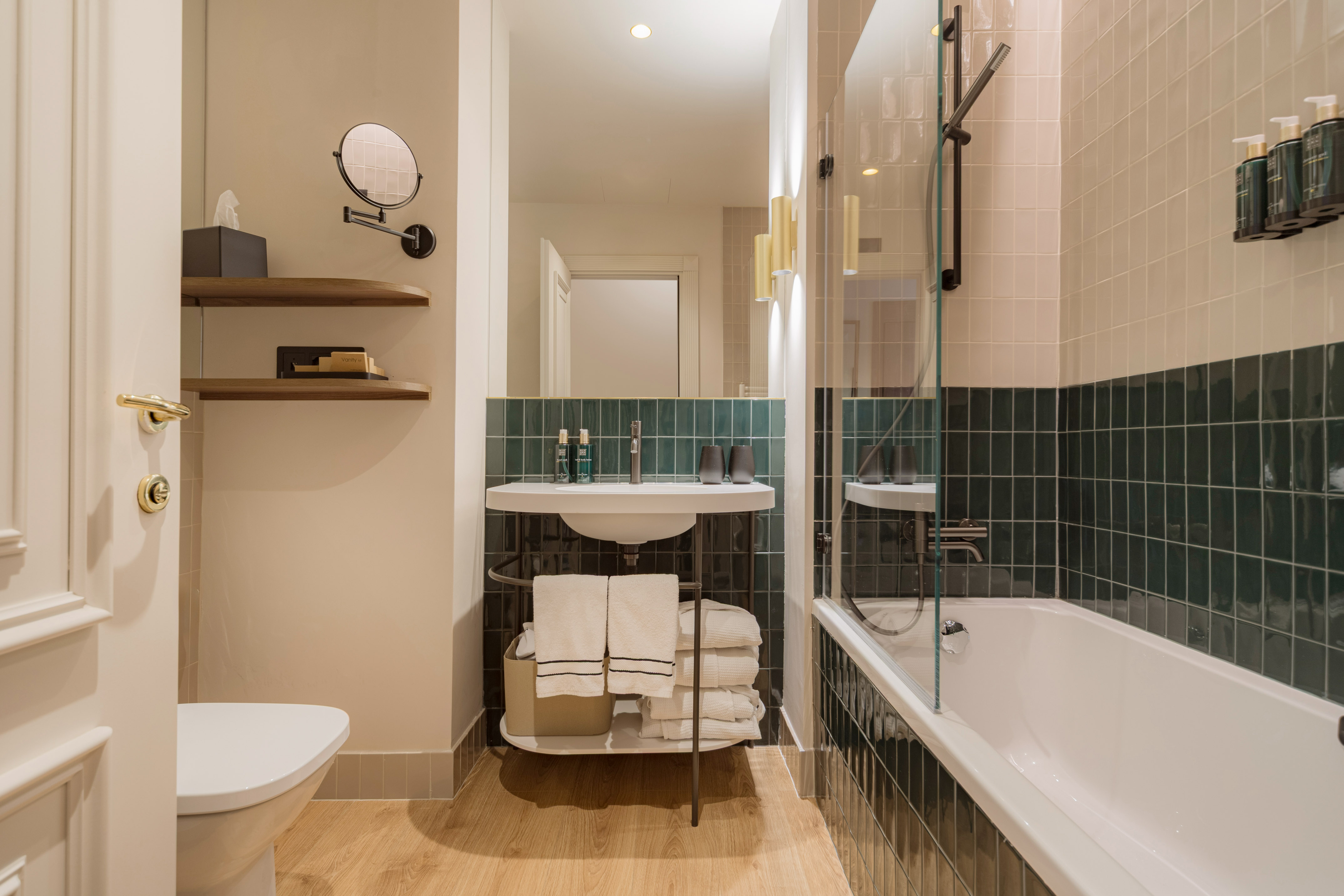 Stylish bathroom with dark green tiles, white bathtub, vanity, and wooden floor.
