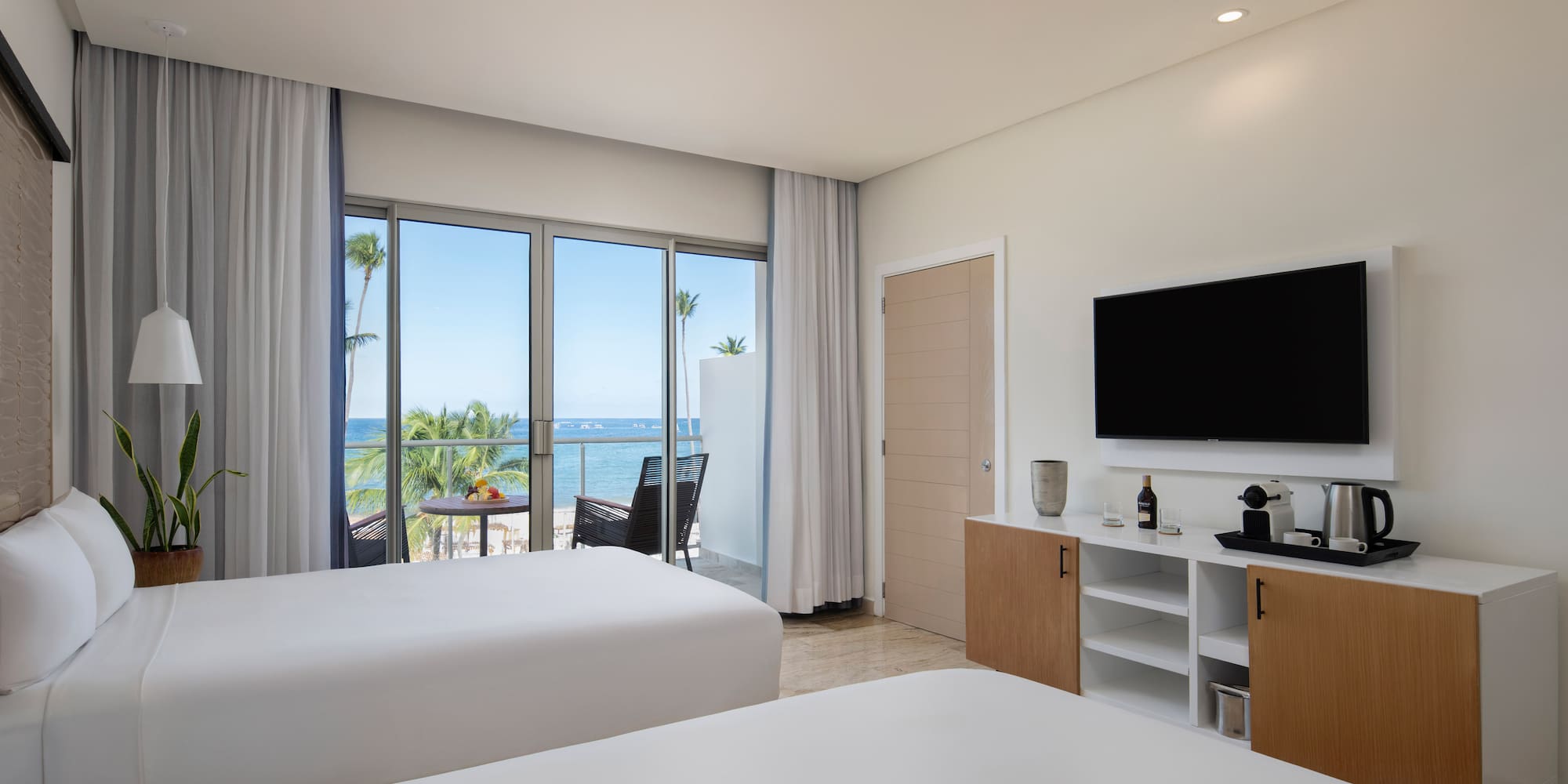 Modern hotel room with two beds, ocean view balcony, and beach resort.