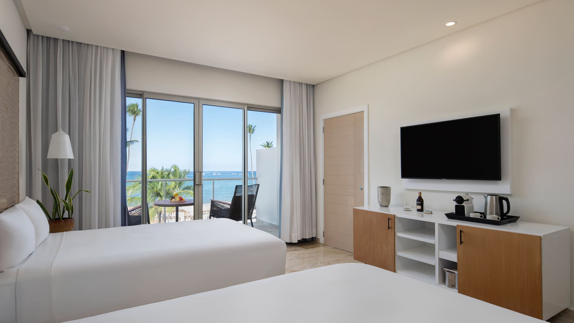 Modern hotel room with two beds, ocean view balcony, and beach resort.