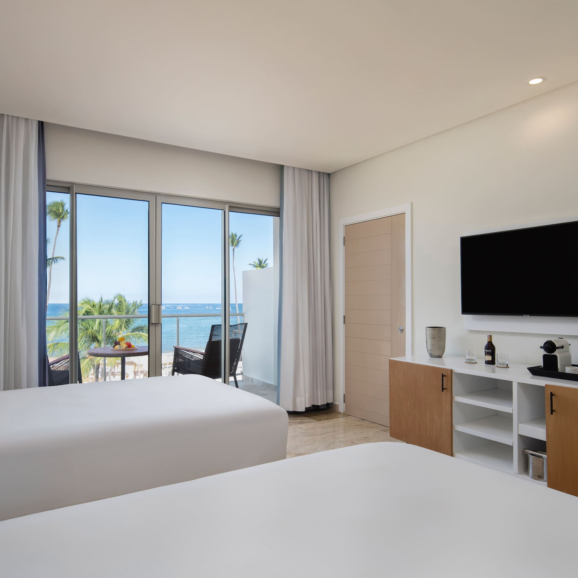 Modern hotel room with two beds, ocean view balcony, and beach resort.