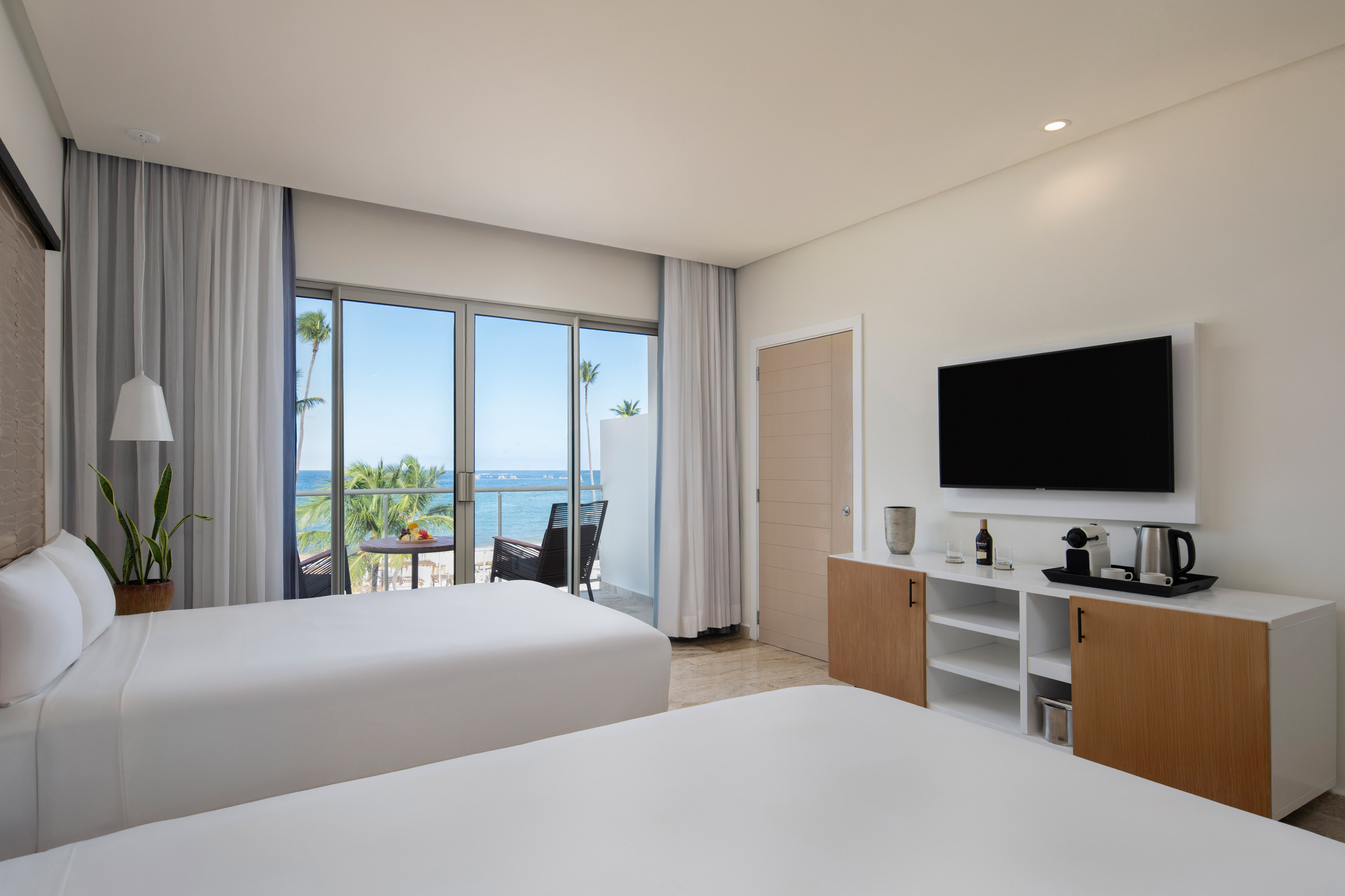 Modern hotel room with two beds, ocean view balcony, and beach resort.