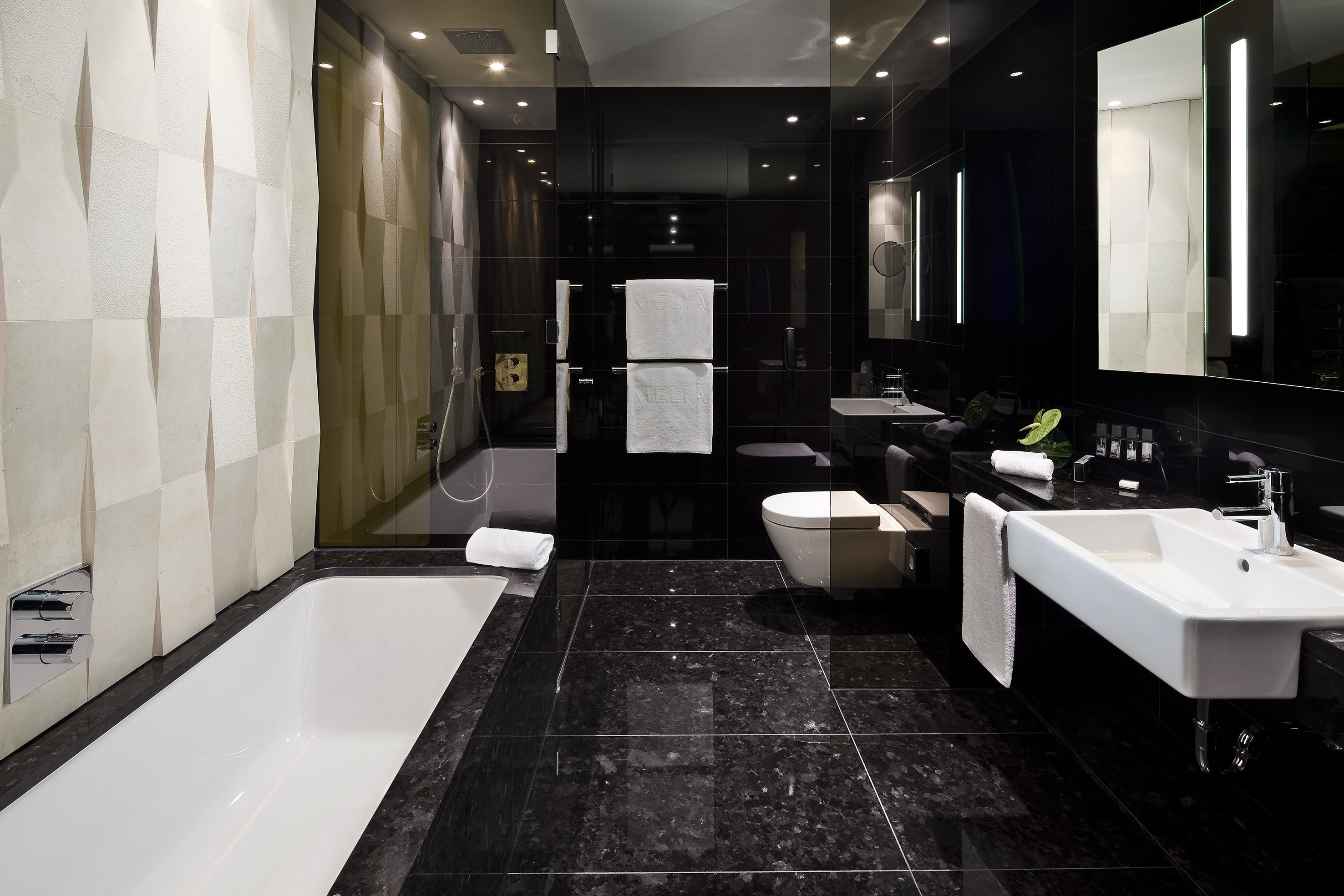 Modern hotel bathroom with black granite, white tub, sink, and textured wall.