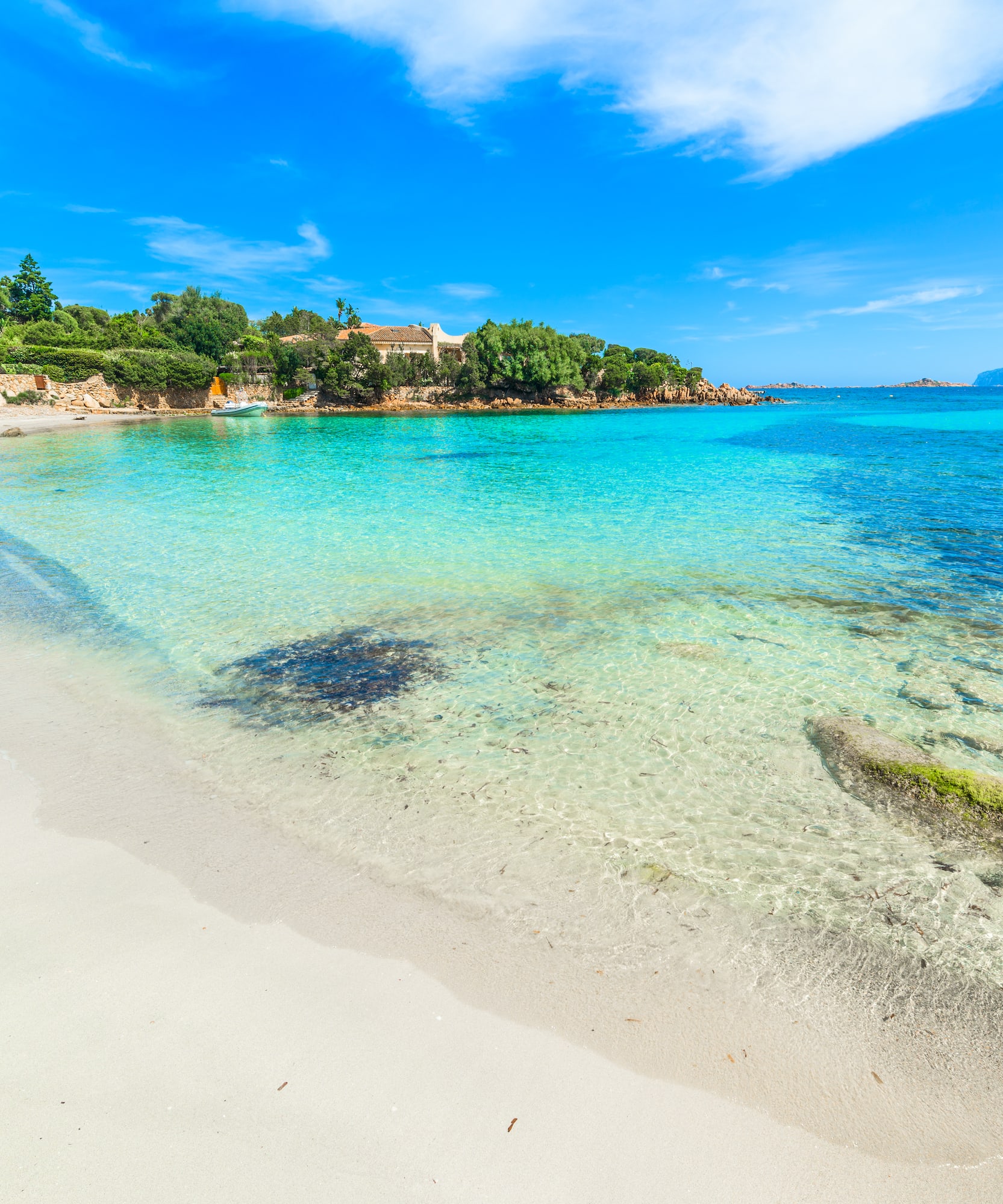 White sand beach with clear turquoise water, lush green coastline, blue sky.