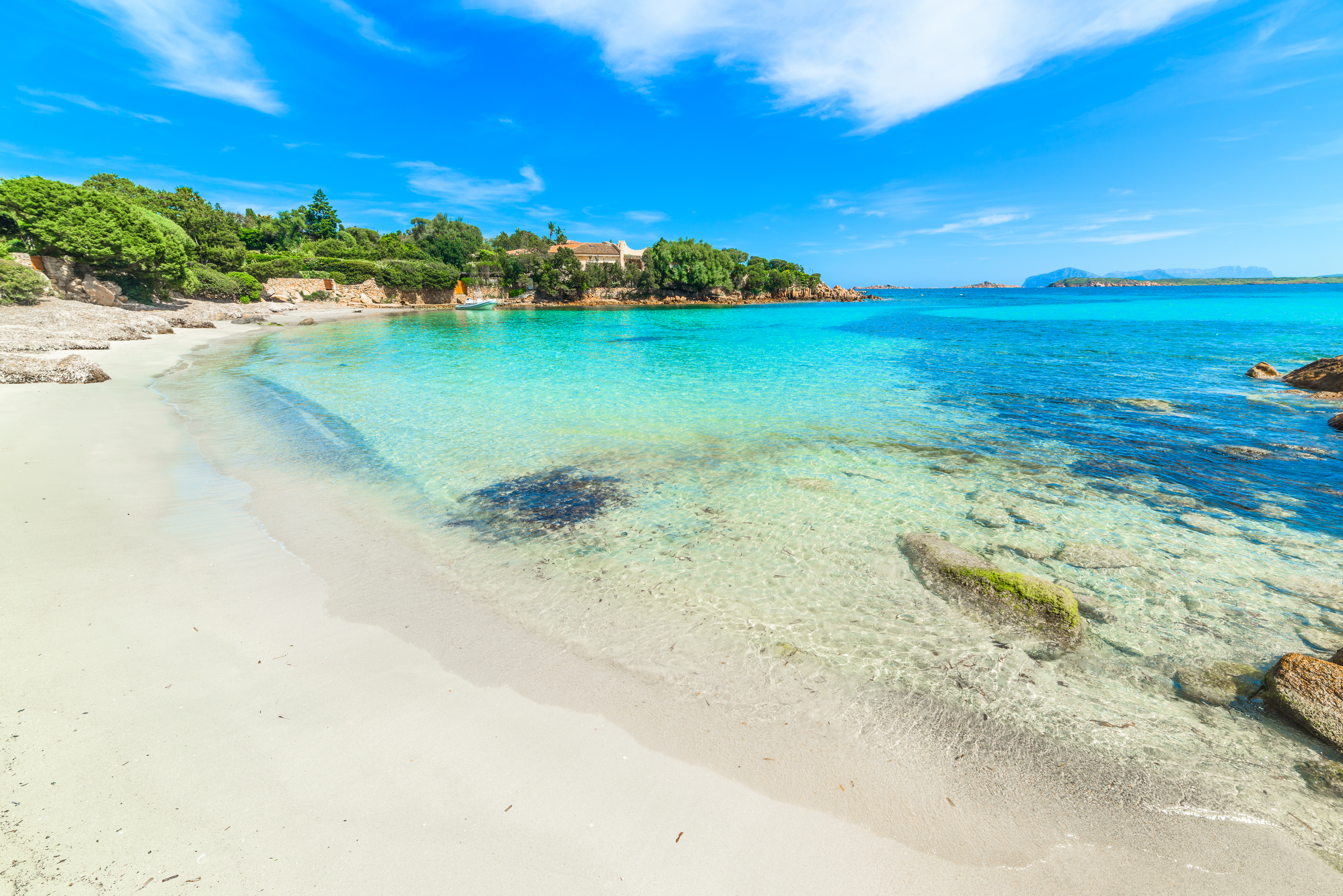 White sand beach with clear turquoise water, lush green coastline, blue sky.