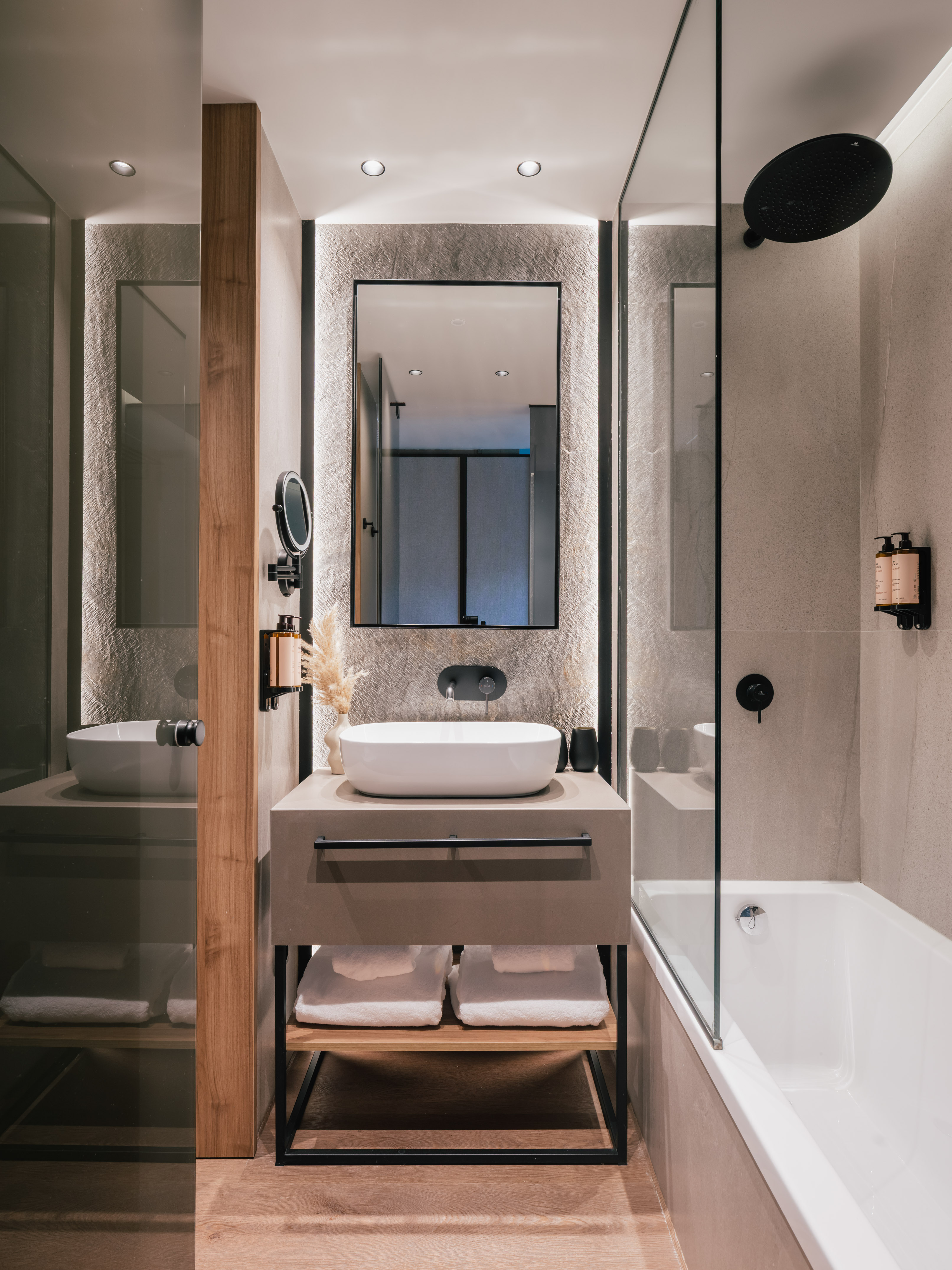Modern bathroom with sleek vanity, vessel sink, textured wall, and bathtub shower.