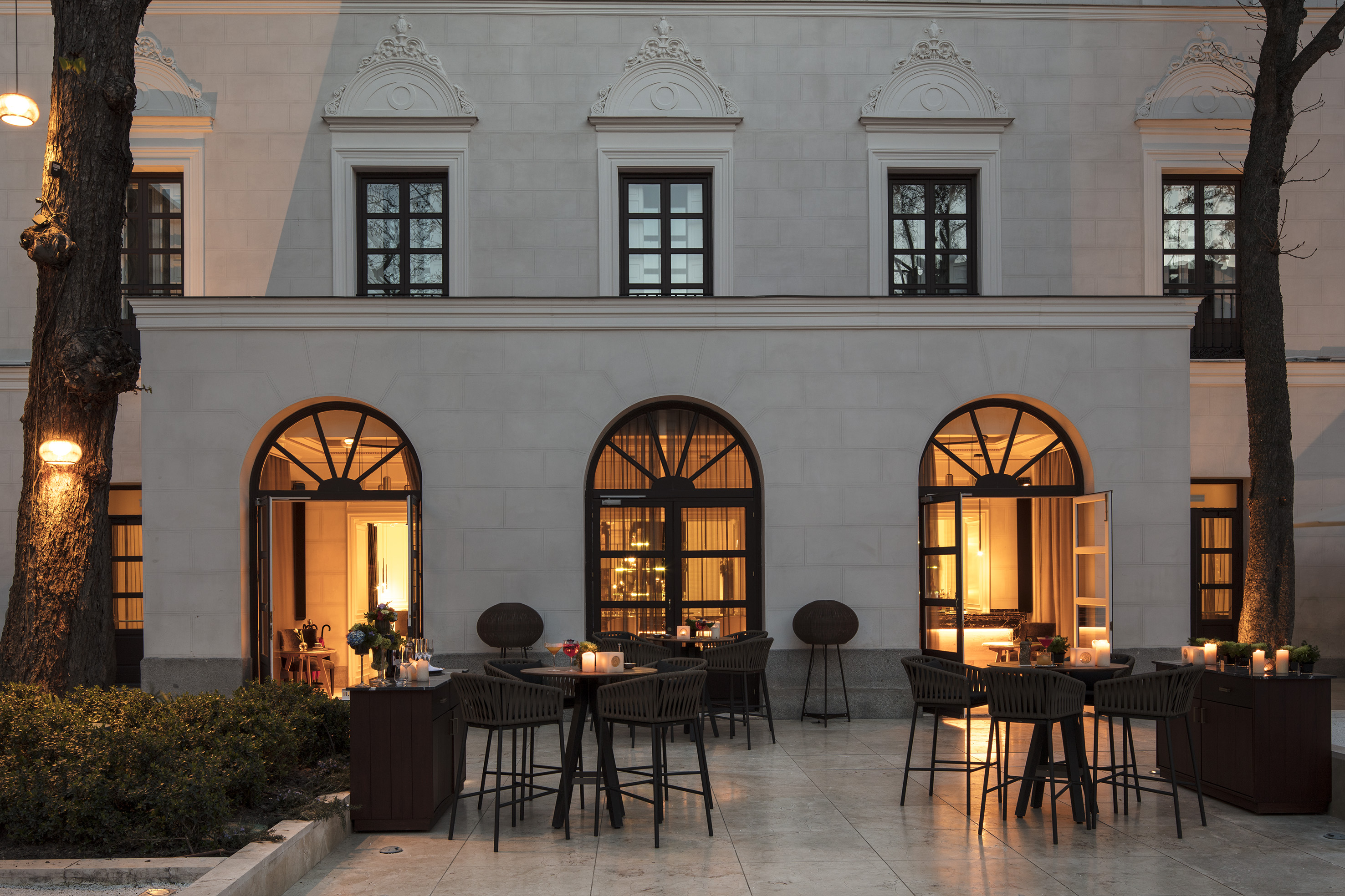 Elegant outdoor patio lounge with stylish seating, warm lights, and building facade.