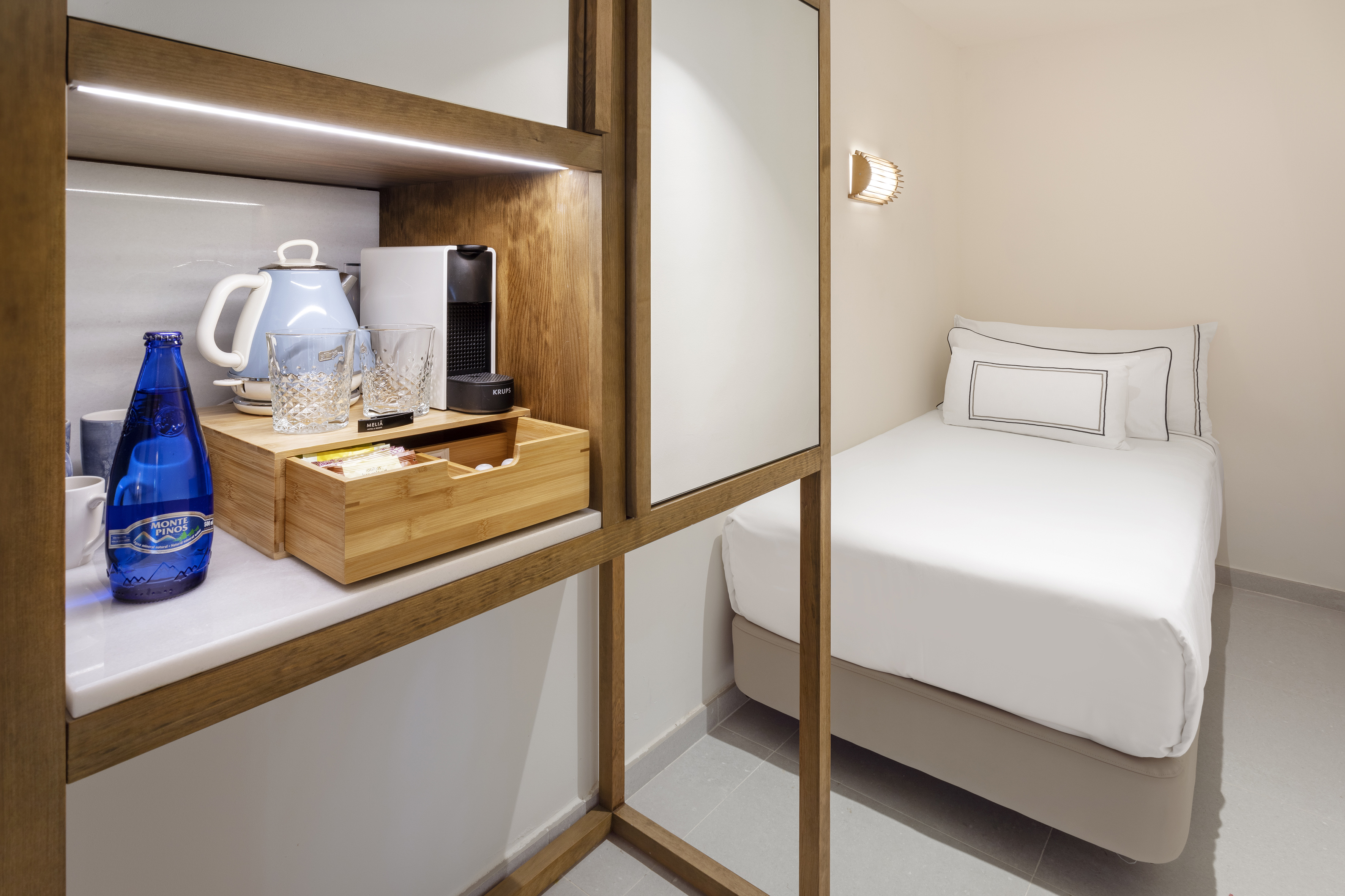 Hotel room with coffee station, blue kettle, coffee machine, and white single bed.