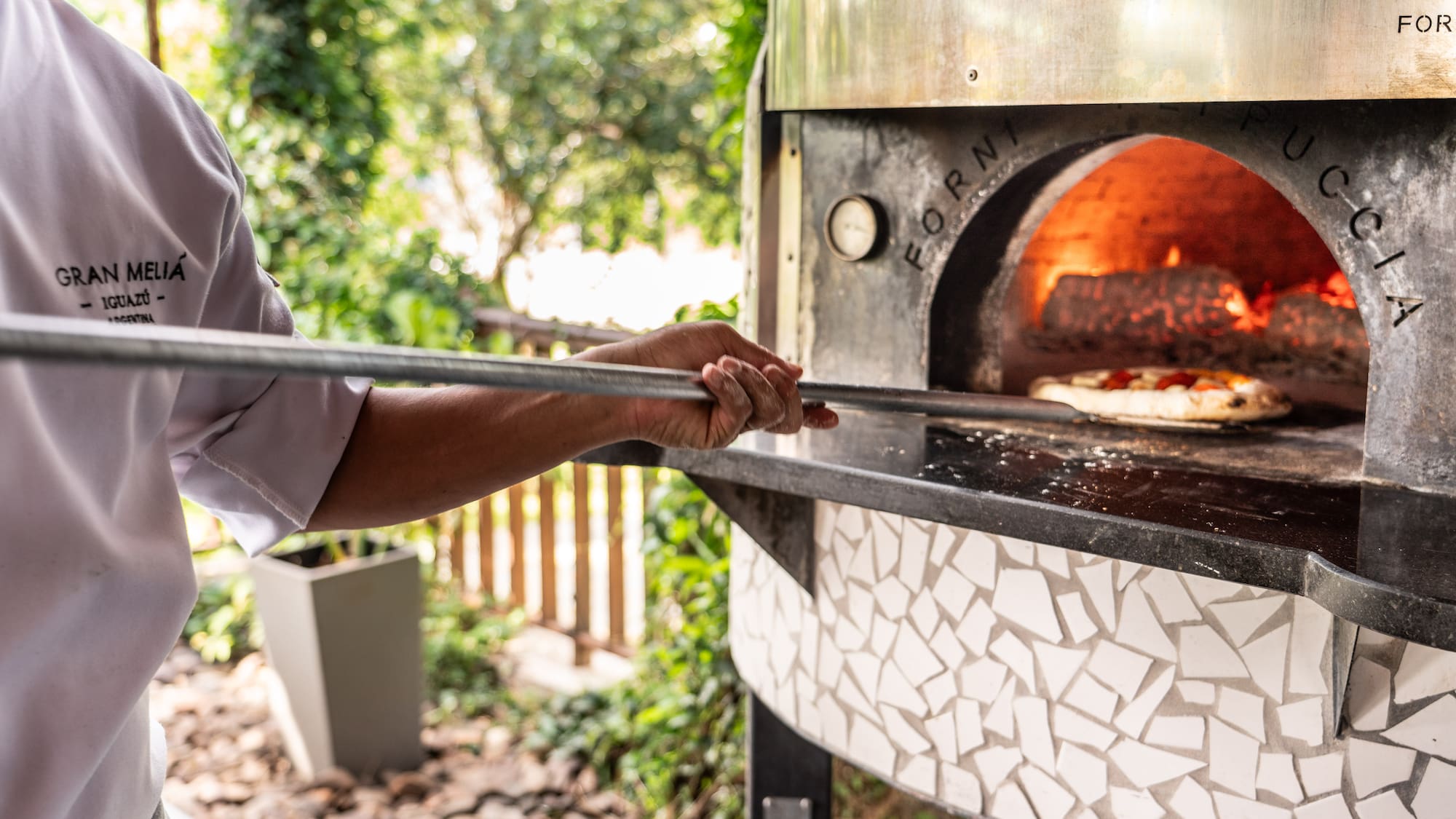 a person holding a stick over a pizza oven