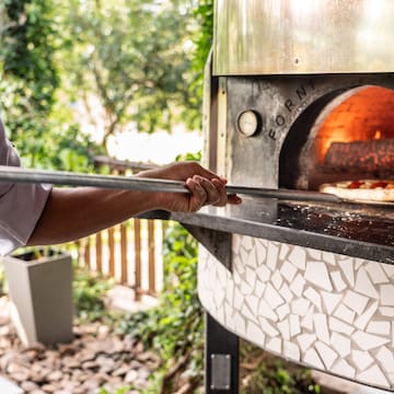 a person holding a stick over a pizza oven