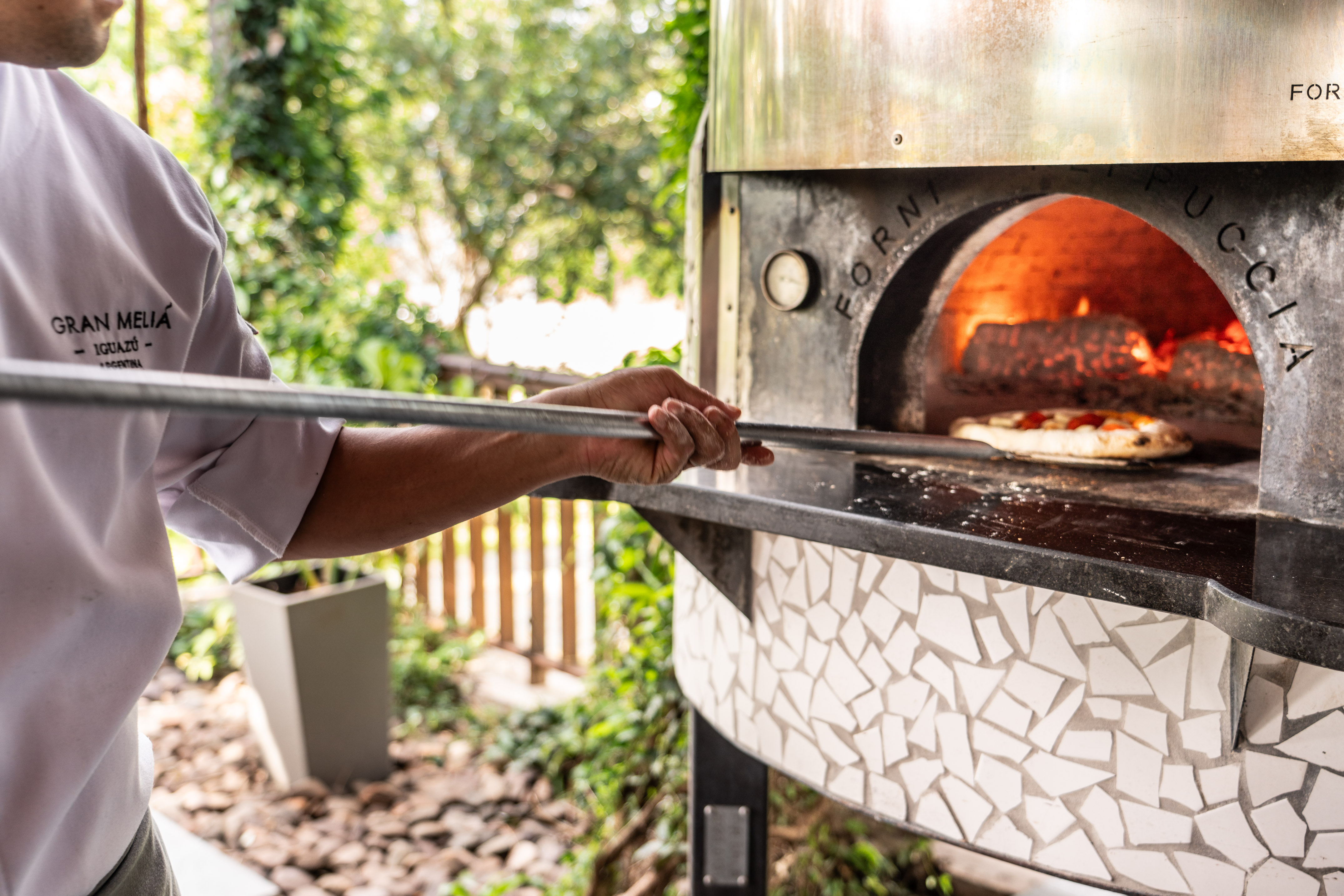 Chef bakes pizza in mosaic wood-fired oven at Gran Melia resort.