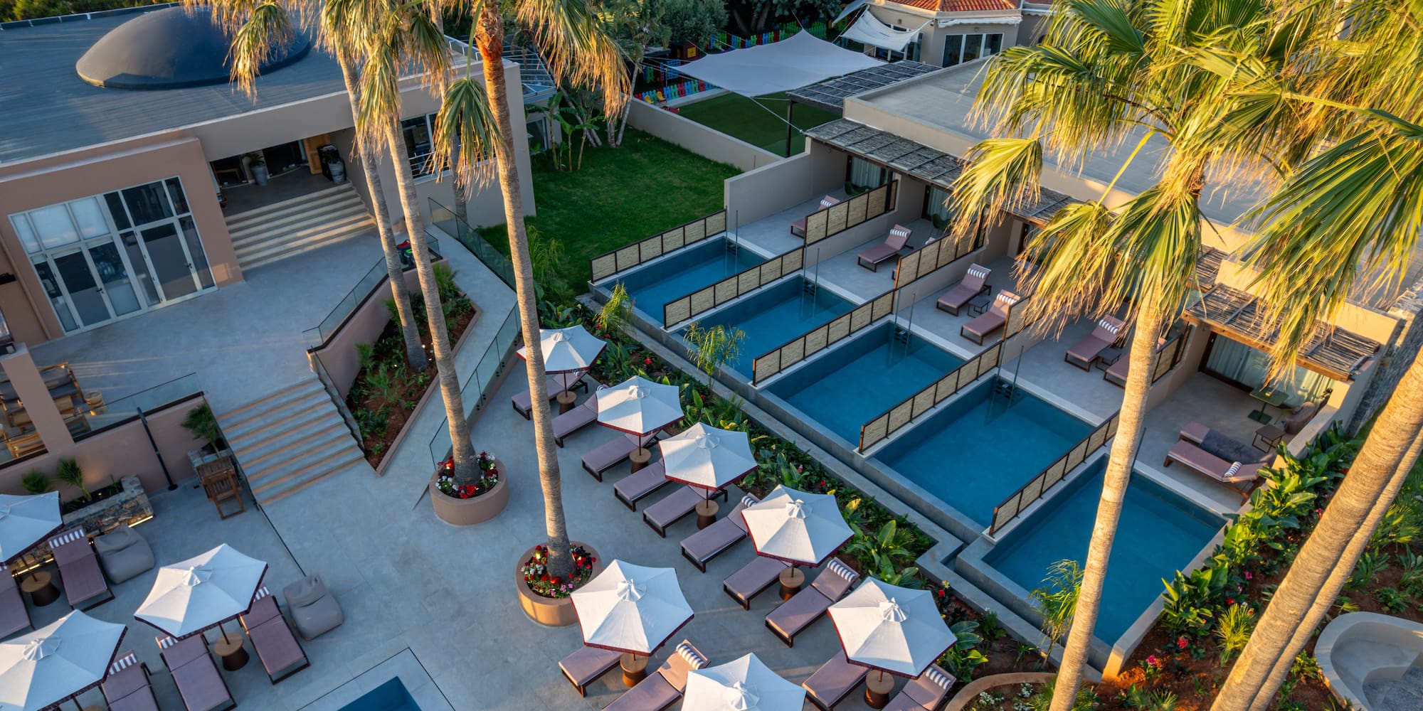 Aerial view: luxury hotel with multiple pools, palm trees, and sun loungers.