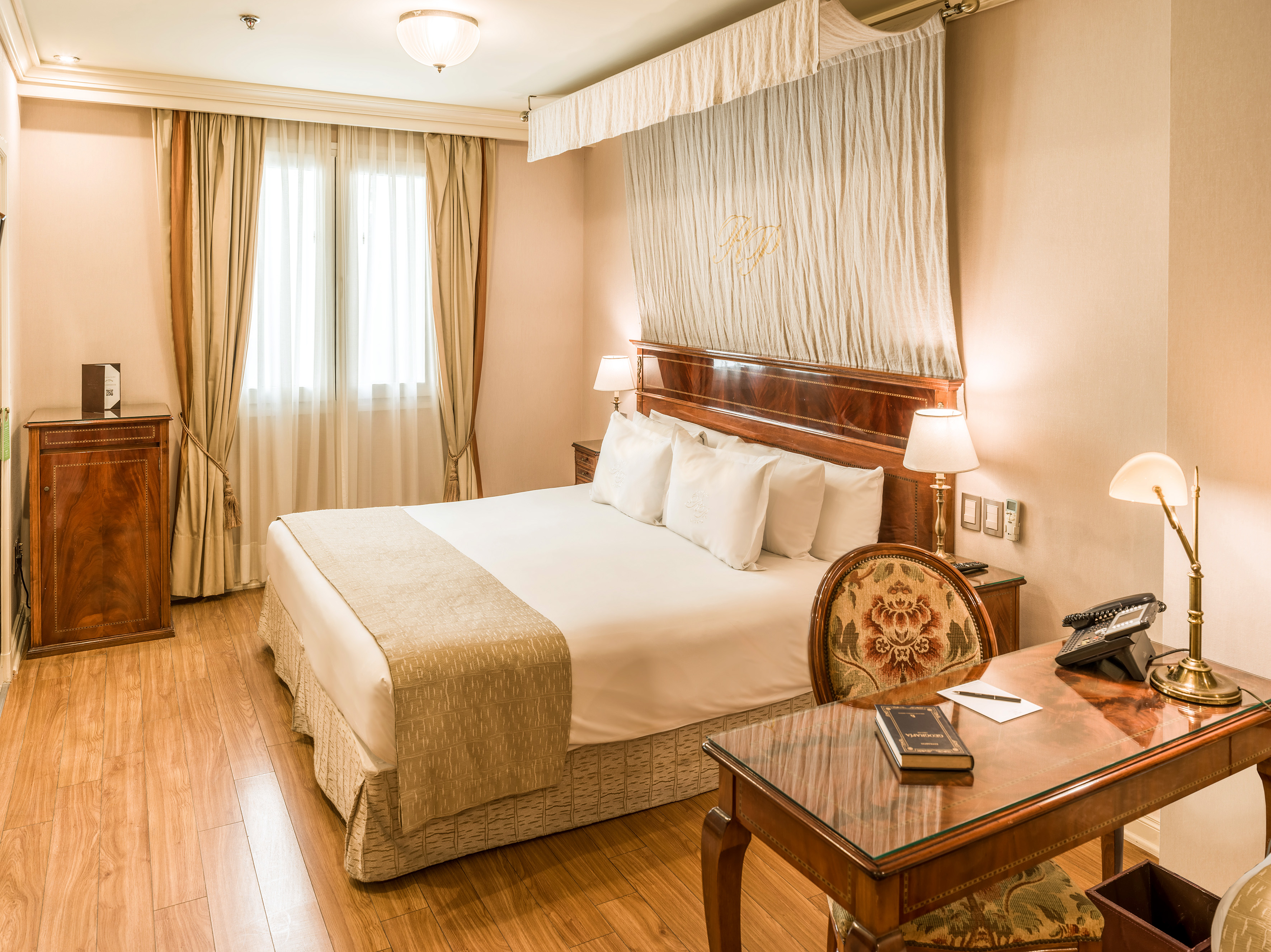 Elegant hotel guest room with king bed, classic wooden desk, and warm decor.
