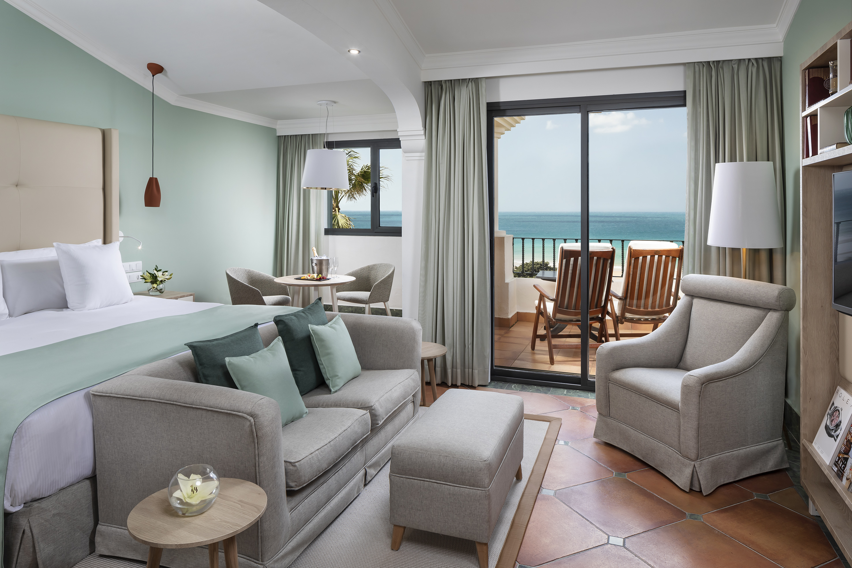 Hotel suite with bed, sofa, private balcony, and ocean view.