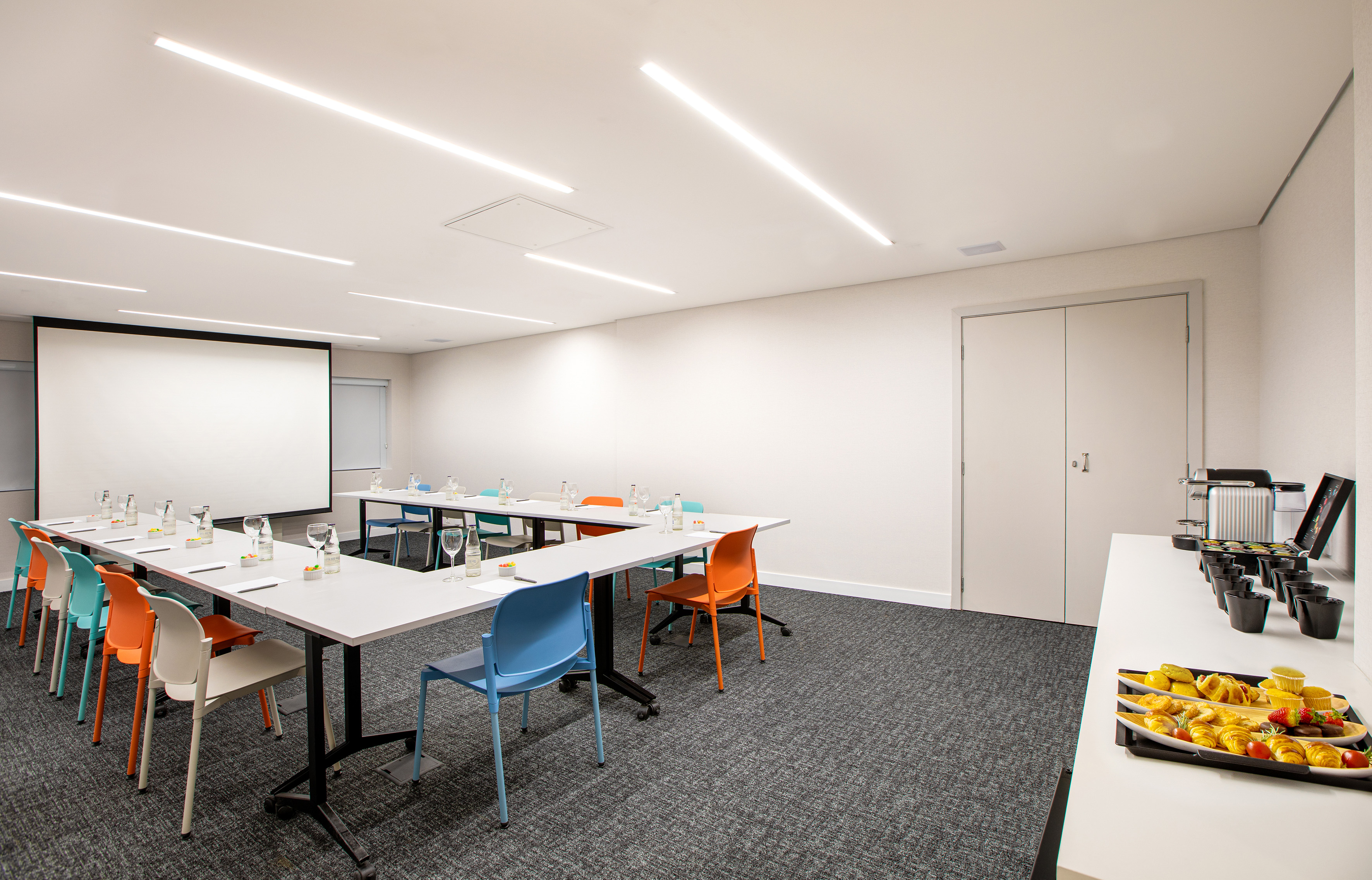 Modern meeting room with projector, colorful U-shaped table, and catering.