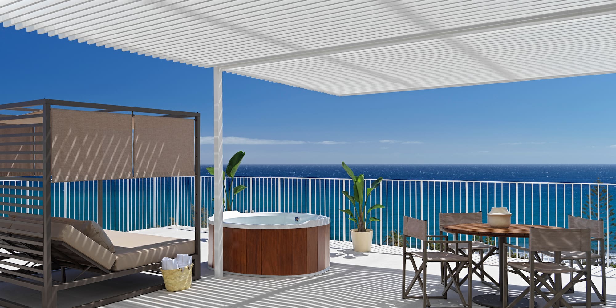 a deck with a hot tub and a table and chairs overlooking the ocean
