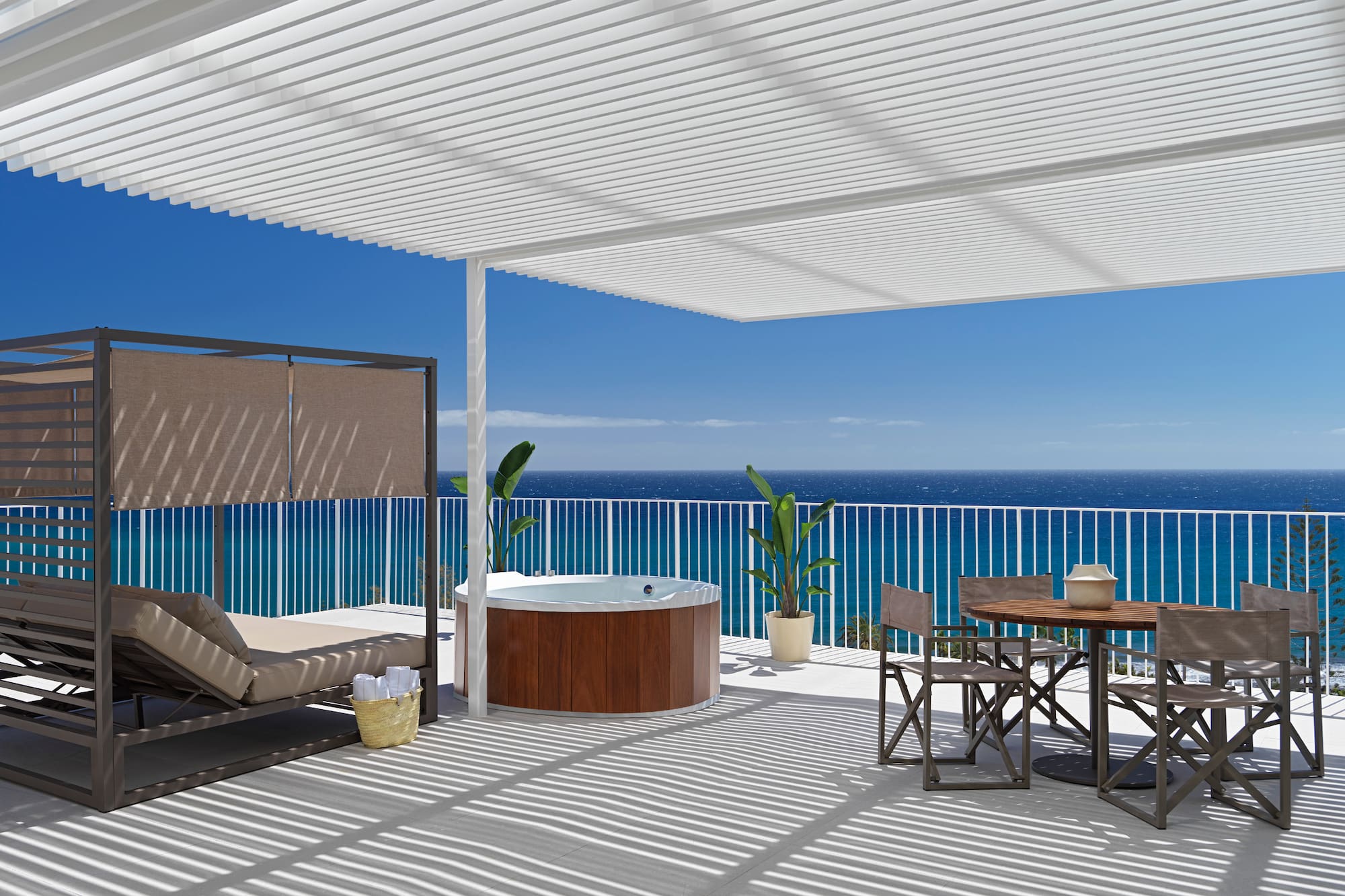 a deck with a hot tub and a table and chairs overlooking the ocean