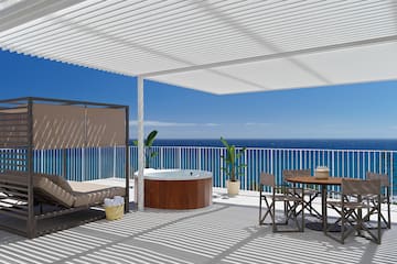 a deck with a hot tub and a table and chairs overlooking the ocean