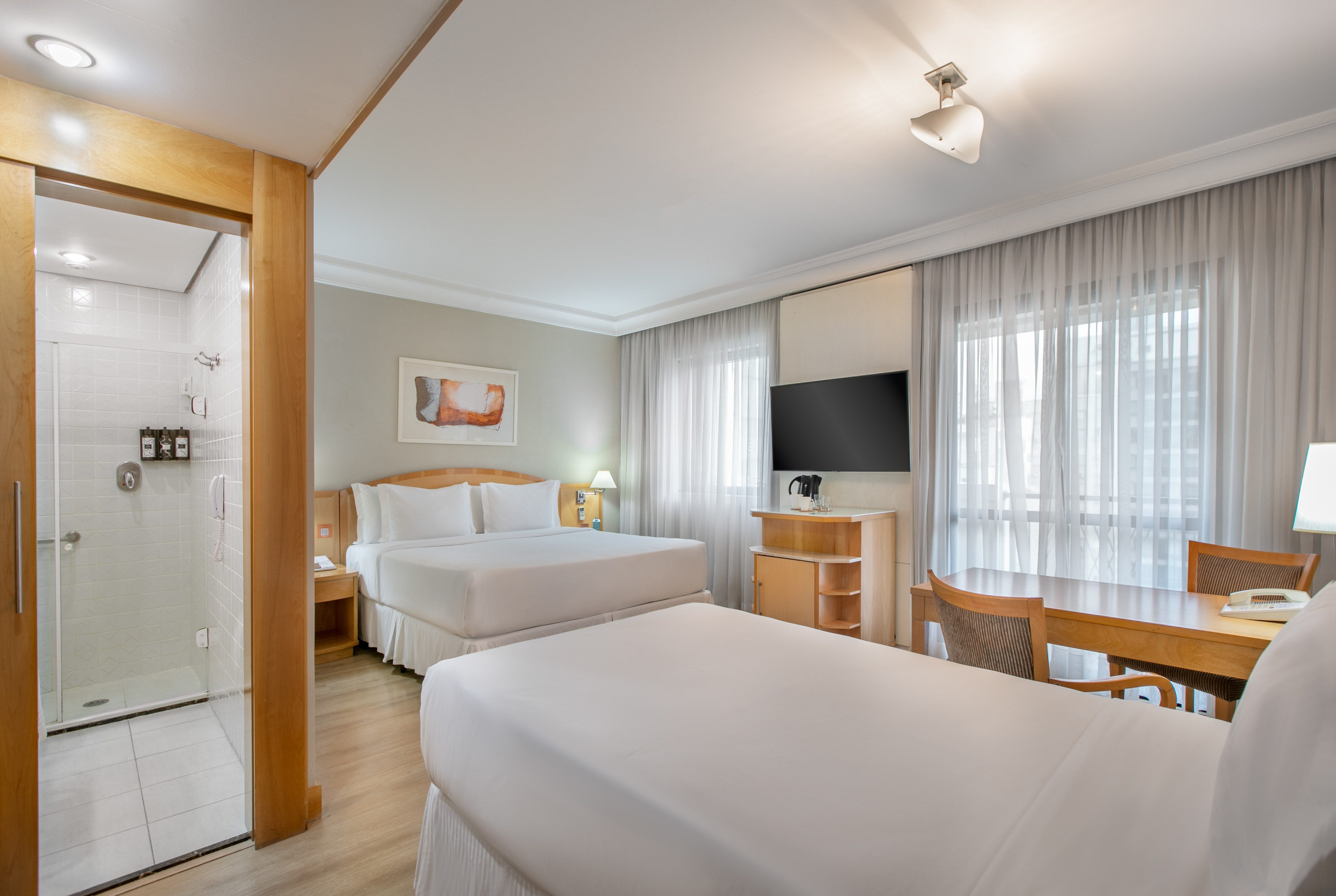 Spacious hotel room with two beds, a walk-in shower, desk, and TV.