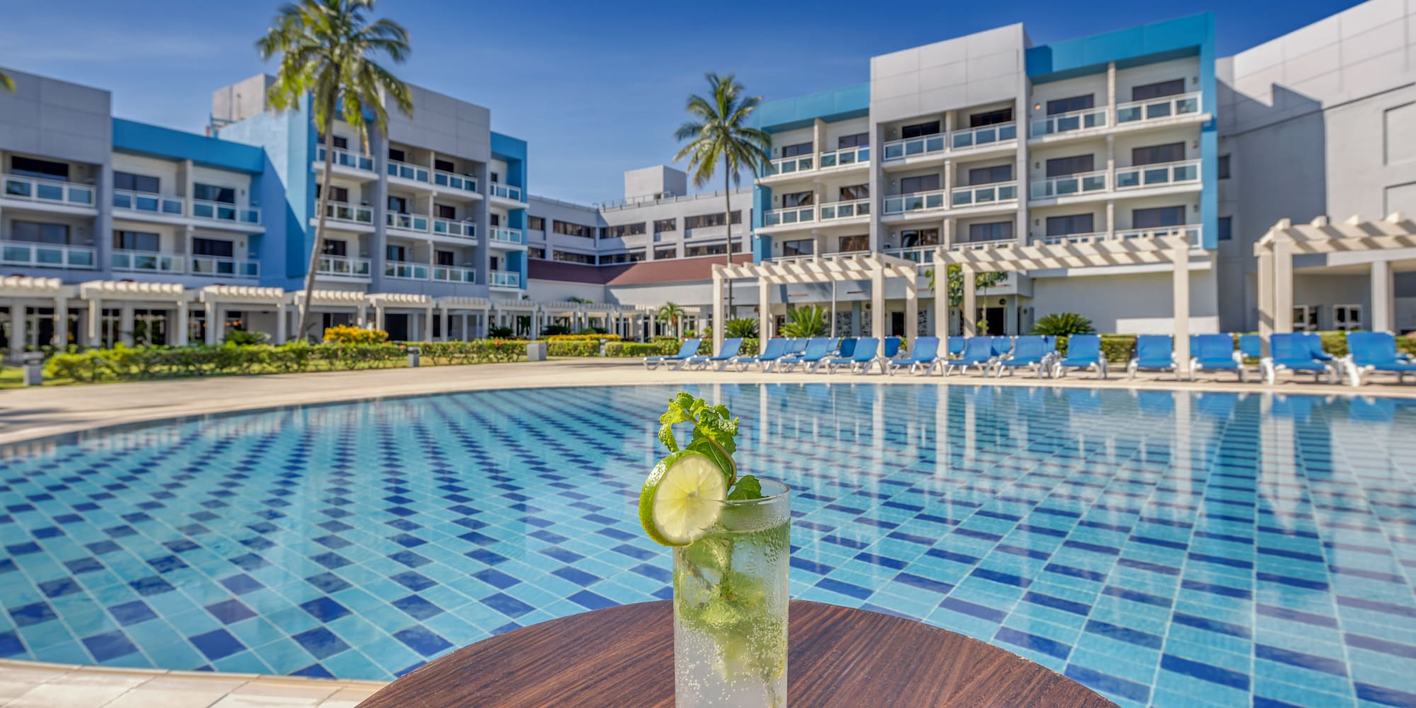 a glass of drink on a table next to a pool