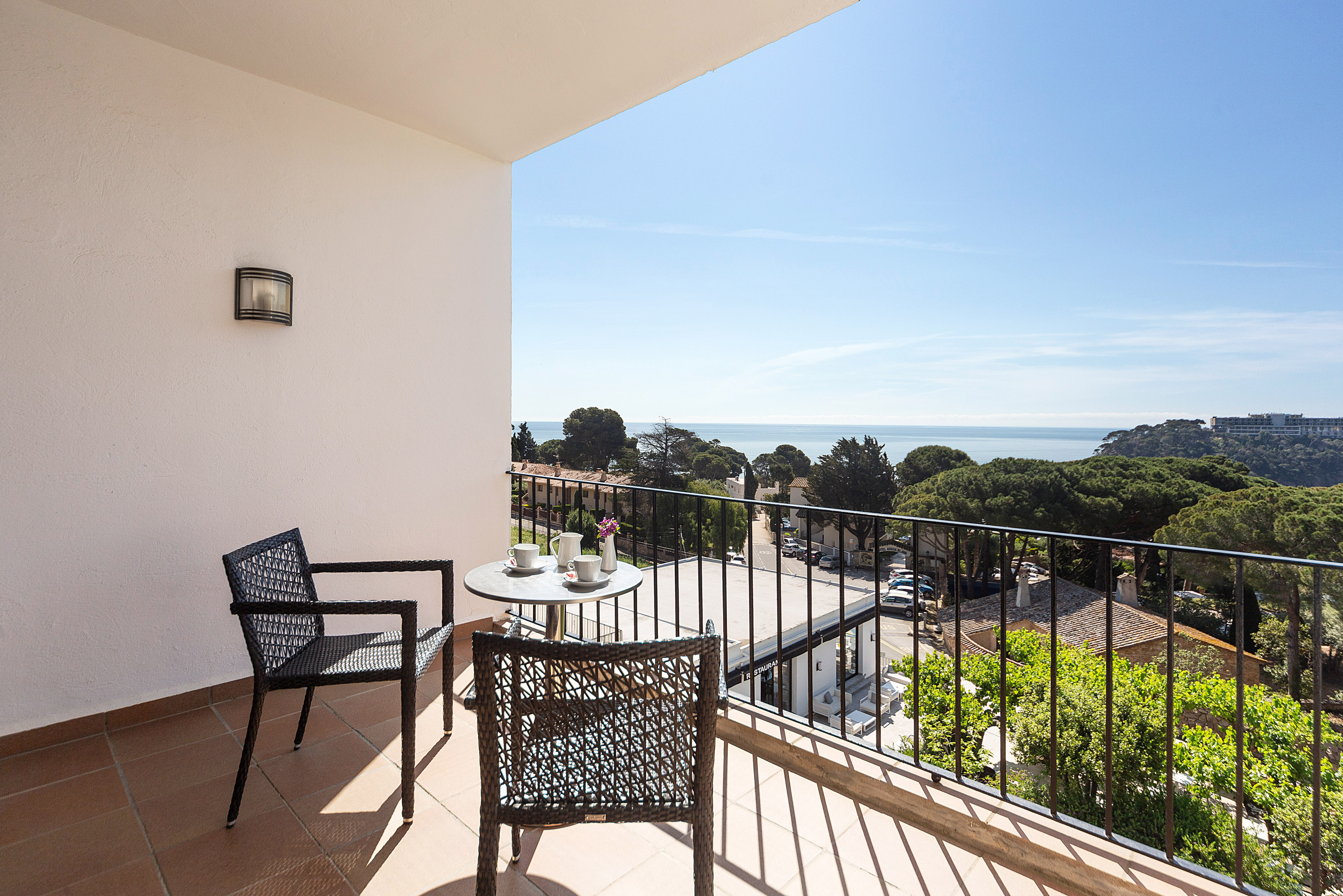 Balcony with outdoor table, chairs, and expansive sea view of coastal town.