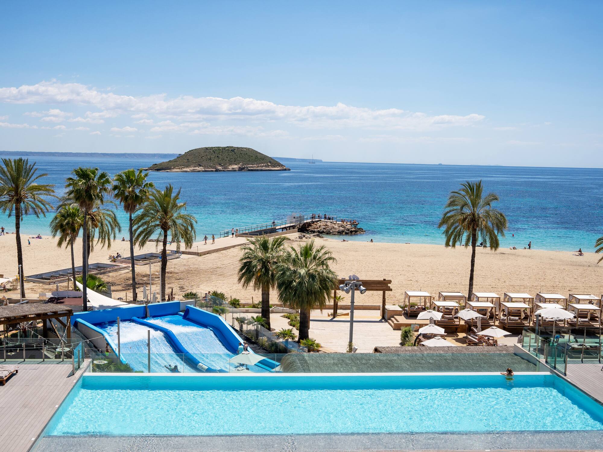 Tropical beach resort: infinity pool, waterslide, palm trees, and ocean.