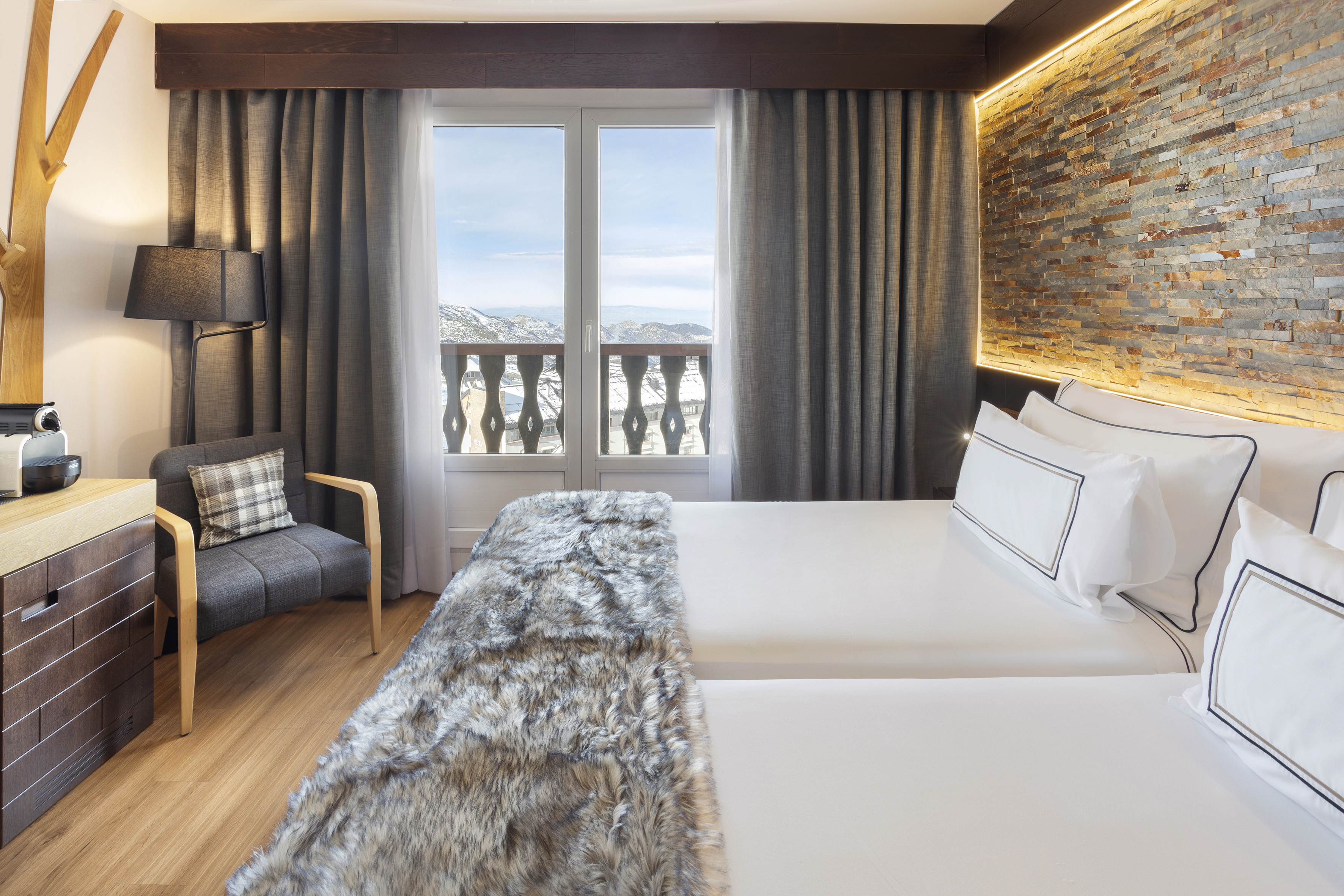 Modern ski resort hotel room with mountain view, faux fur throw, and stone wall.