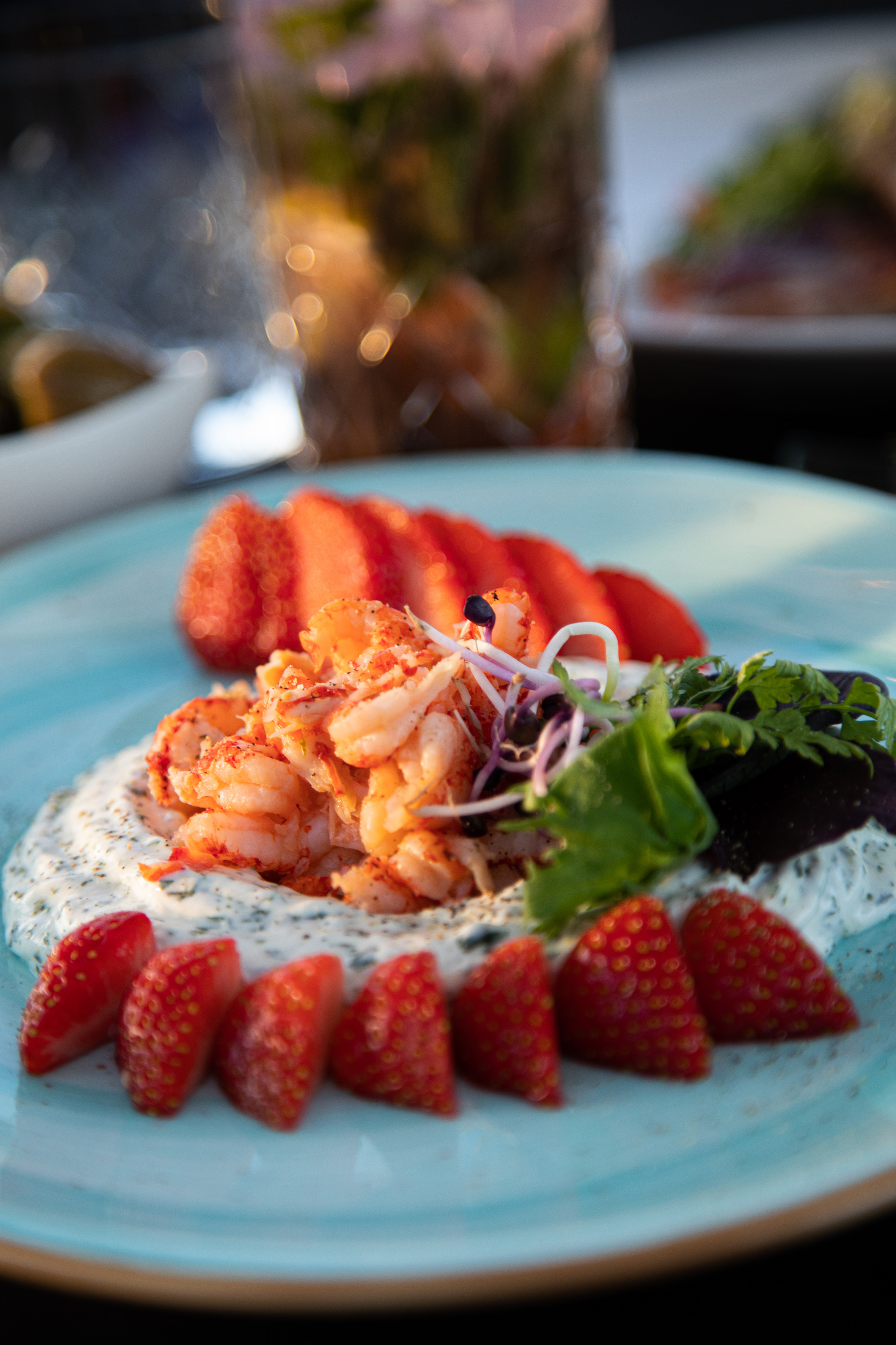 Gourmet lobster and strawberry appetizer with creamy sauce on a blue plate.