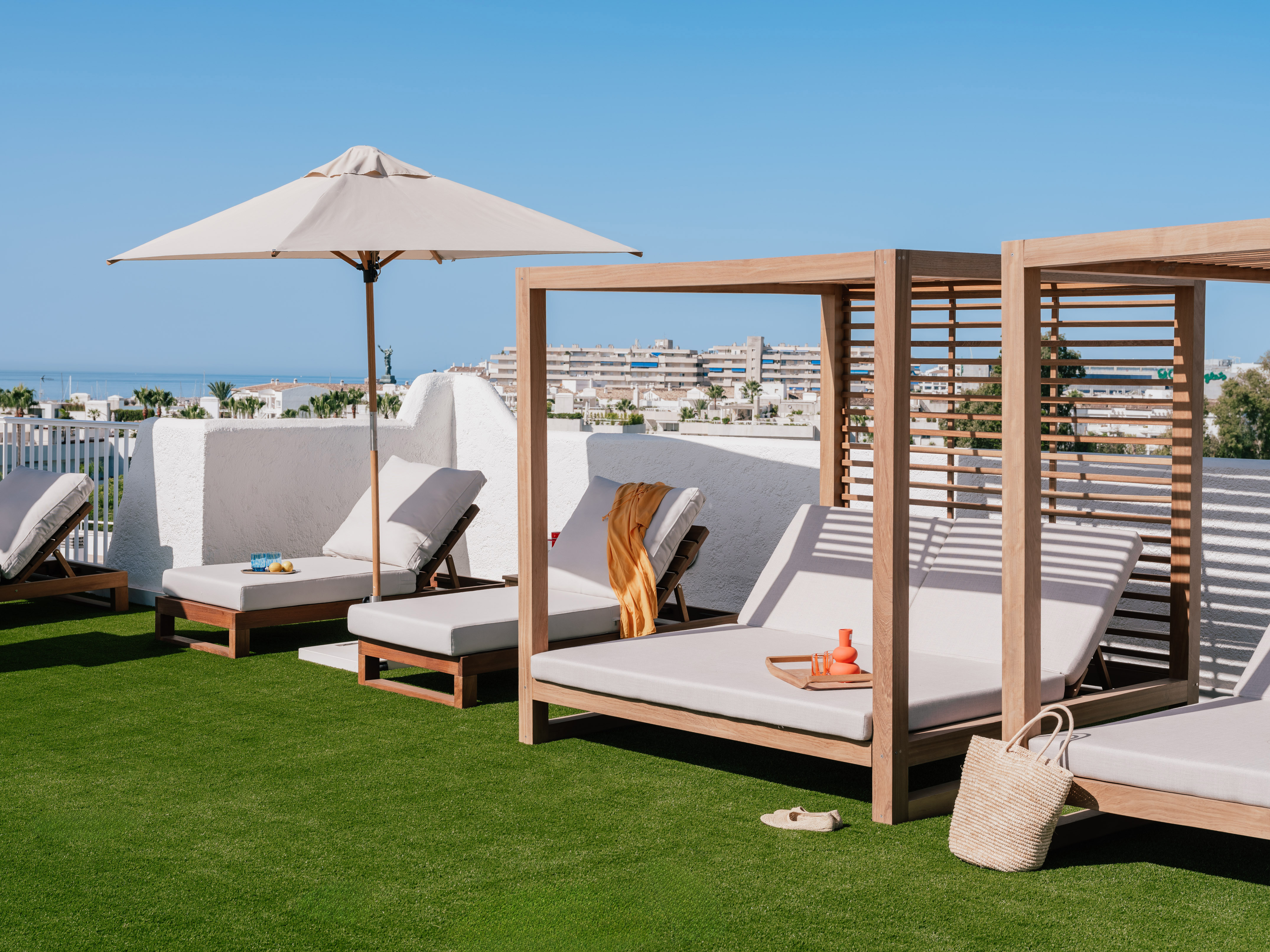 Rooftop resort lounge with modern daybeds, umbrella, ocean view, and green turf.