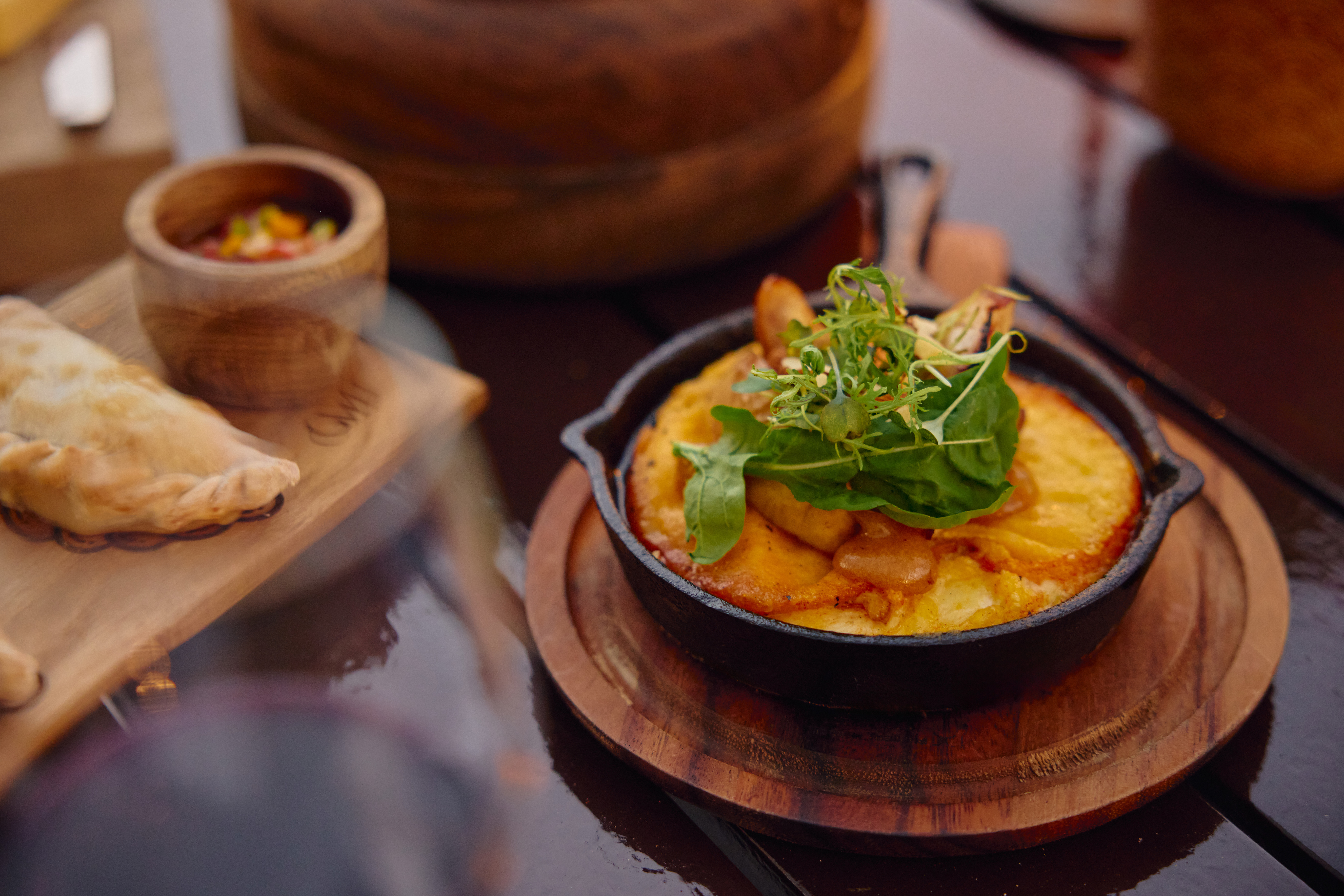 Empanada, gratinado de papas con rúcula fresca y salsa, en mesa rústica.