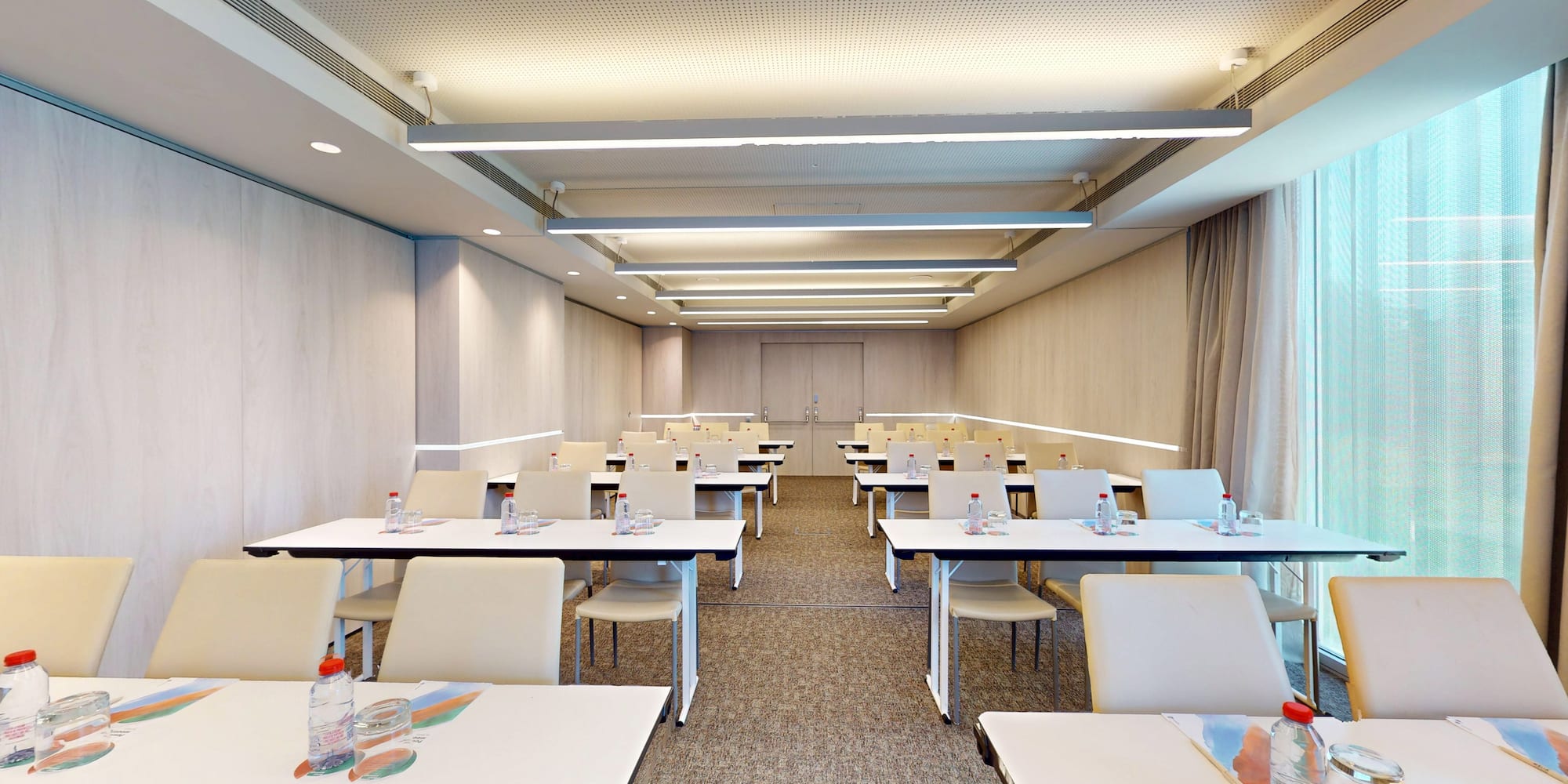 Modern training room with rows of tables, chairs, water, and natural light.