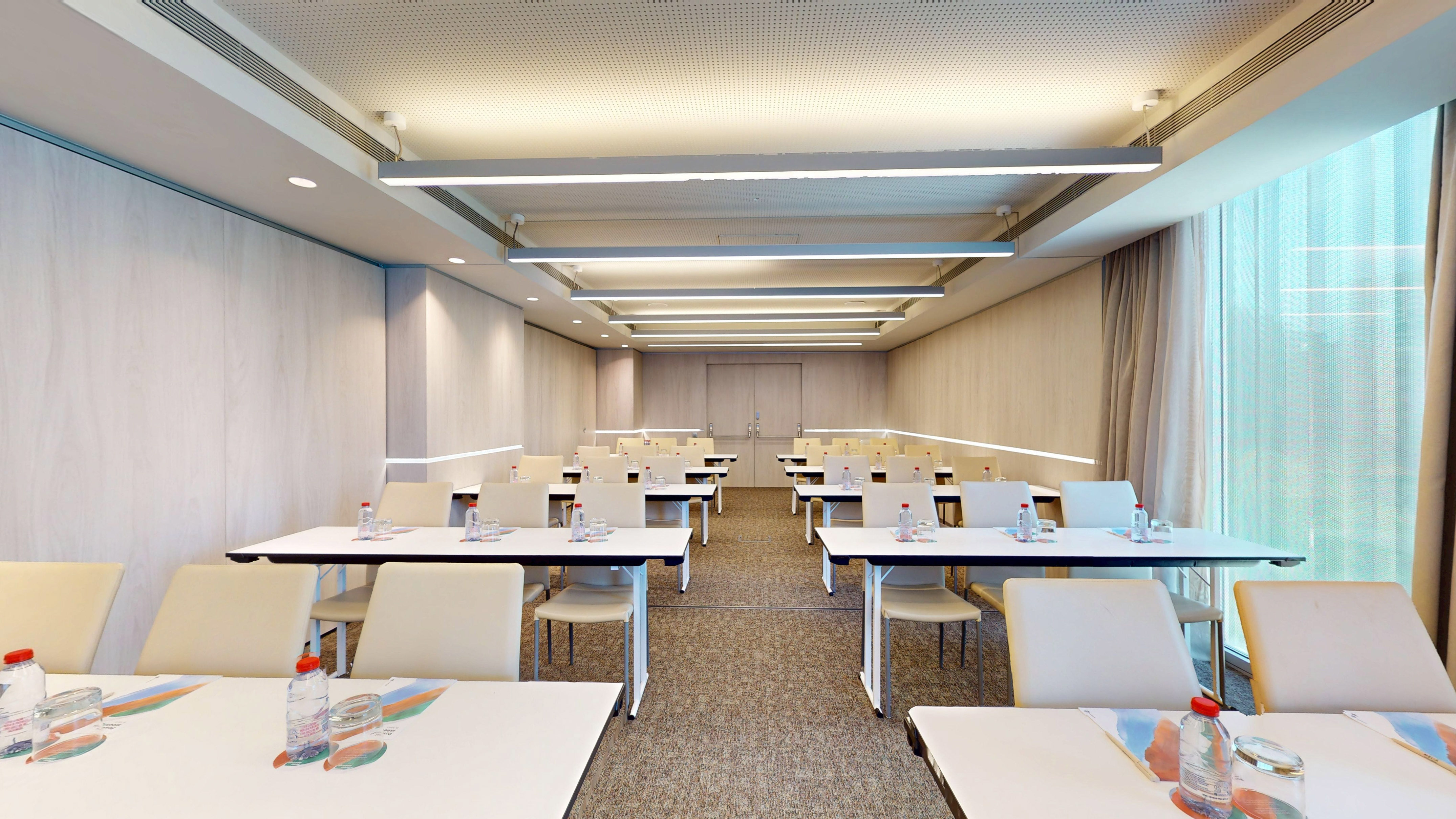 Modern training room with rows of tables, chairs, water, and natural light.