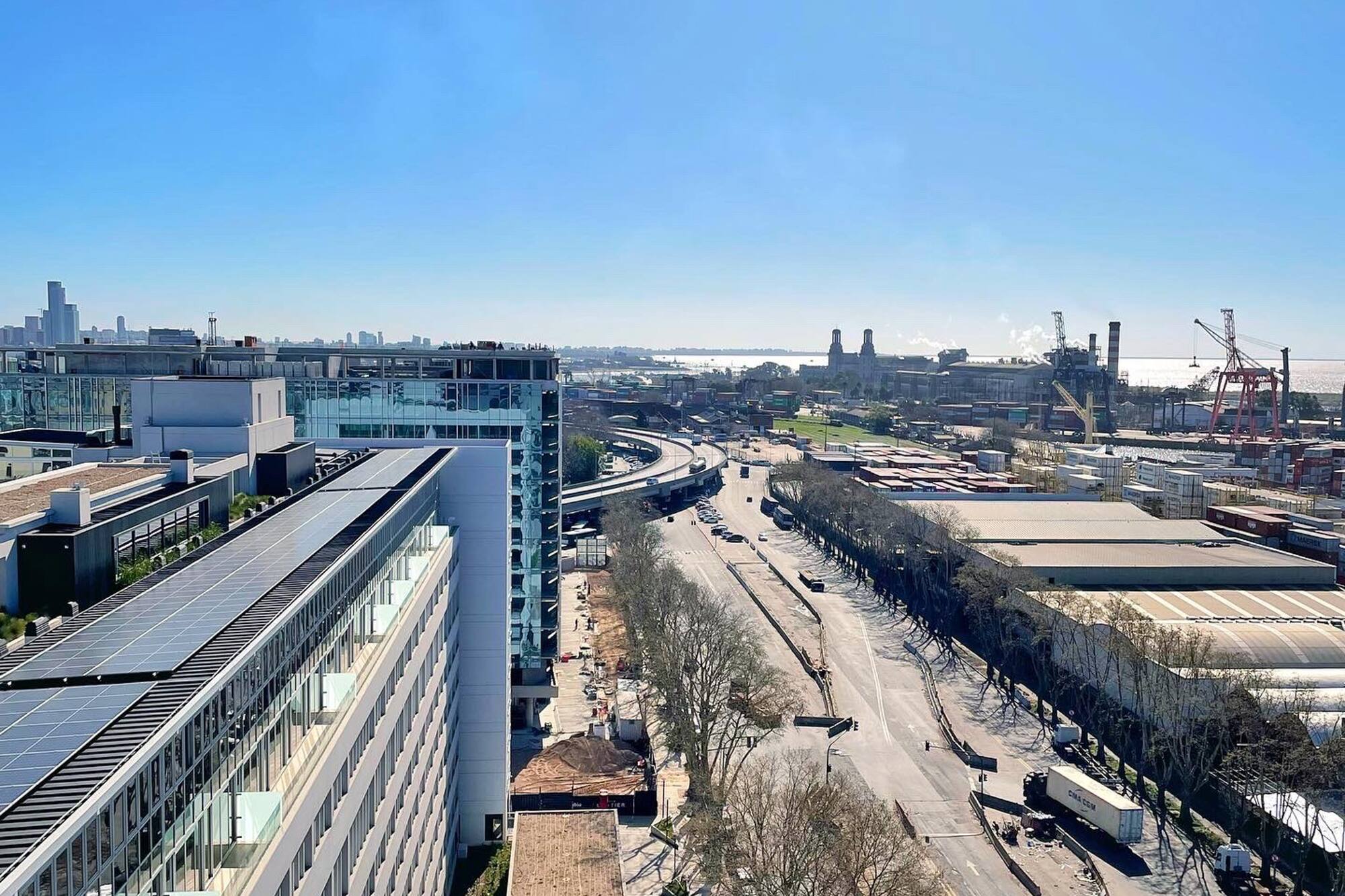 Urban port view: solar panel building, multi-lane highway, industrial cranes.