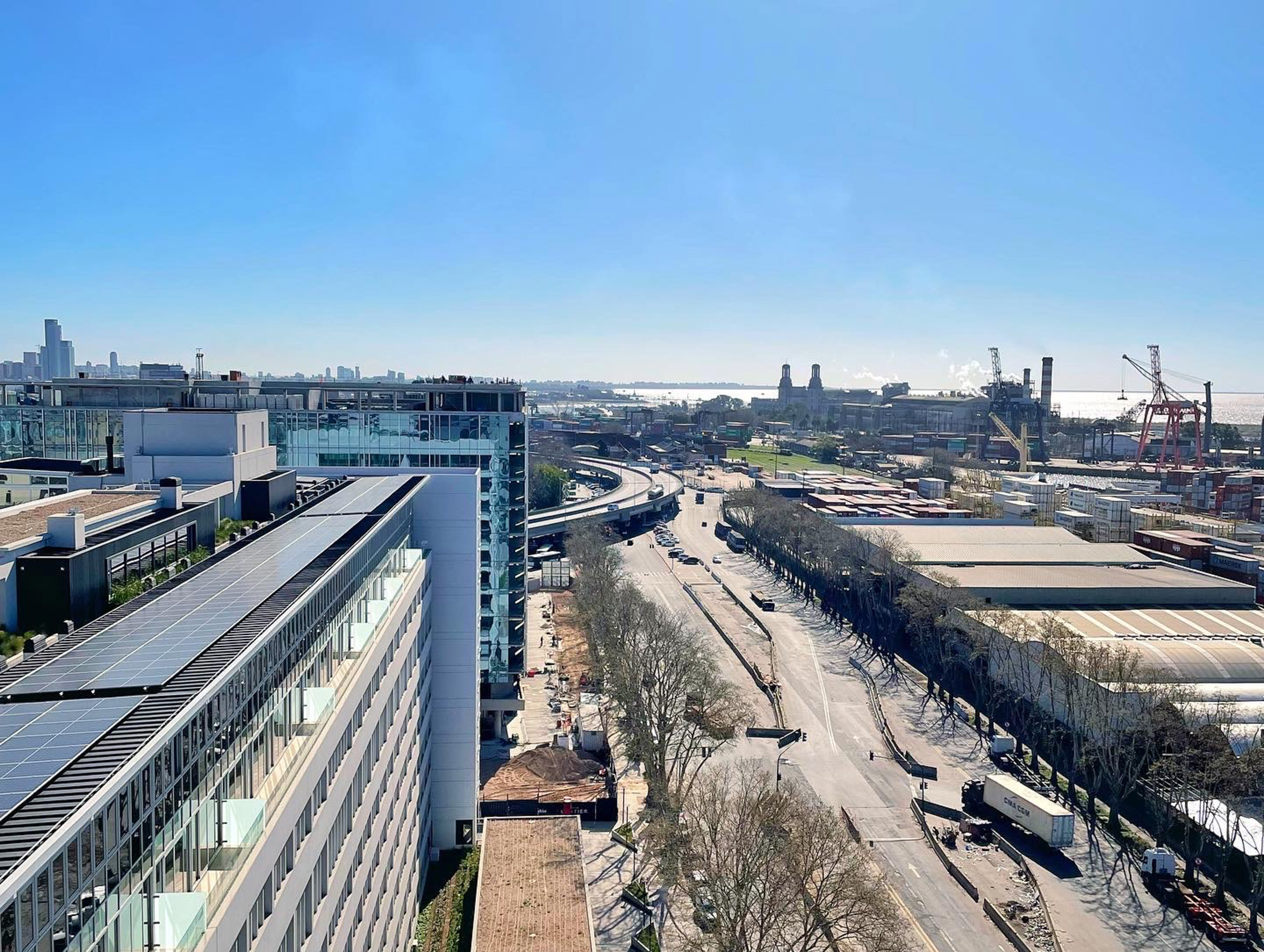 Urban port view: solar panel building, multi-lane highway, industrial cranes.