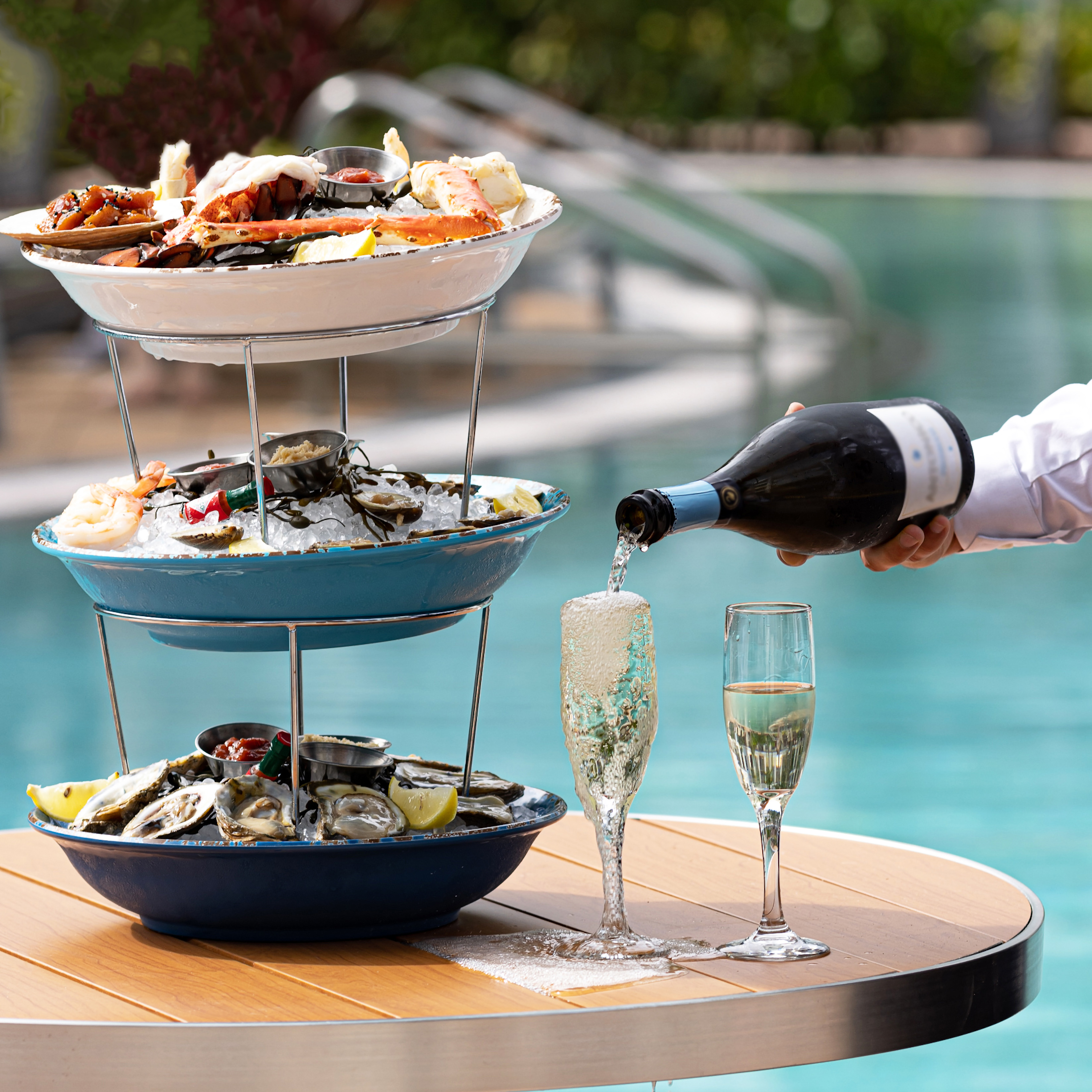 Luxury seafood tower with fresh oysters, lobster, and champagne poured poolside.