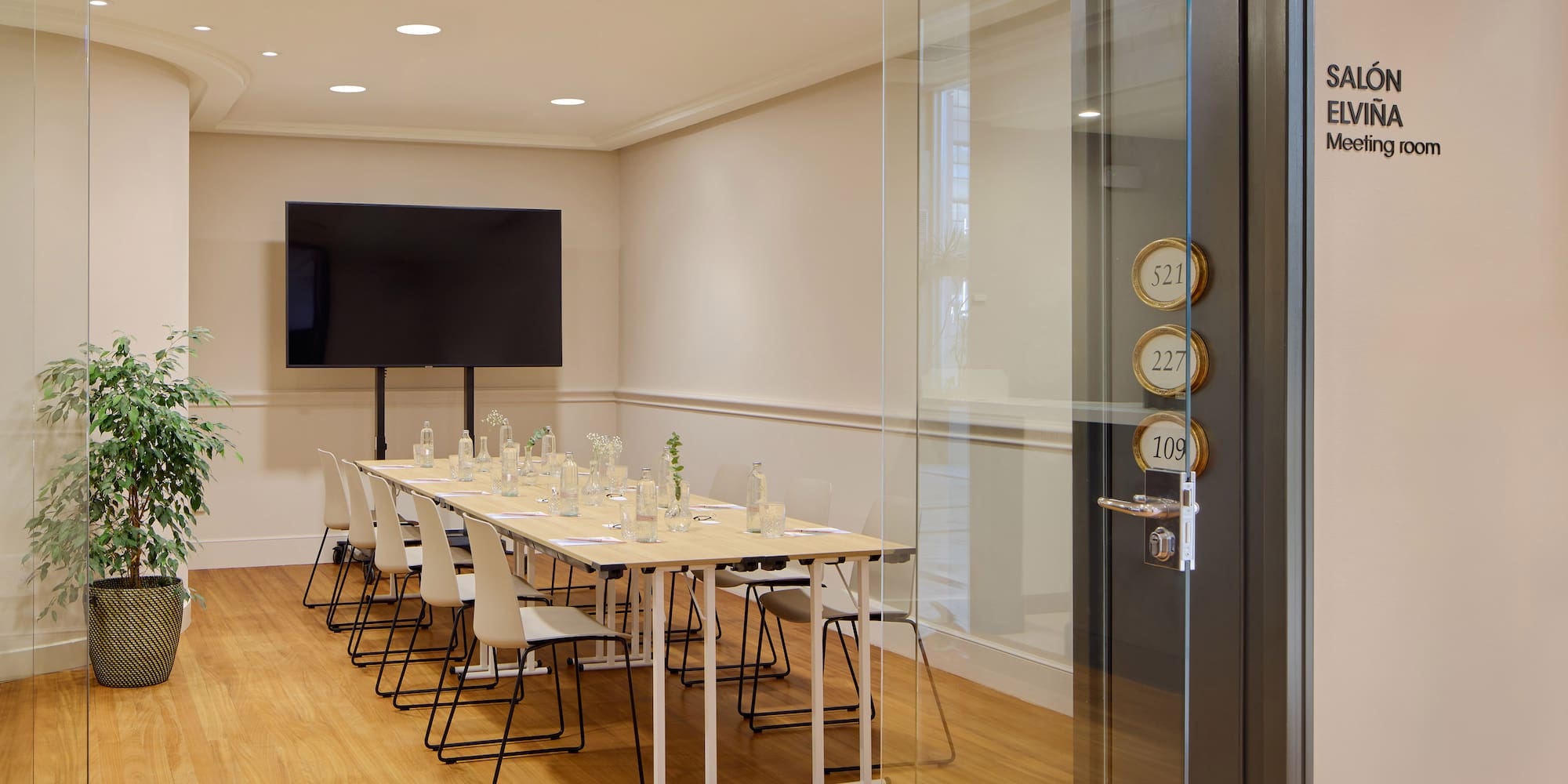 Modern conference room with long table, chairs, large TV, and wooden floor.