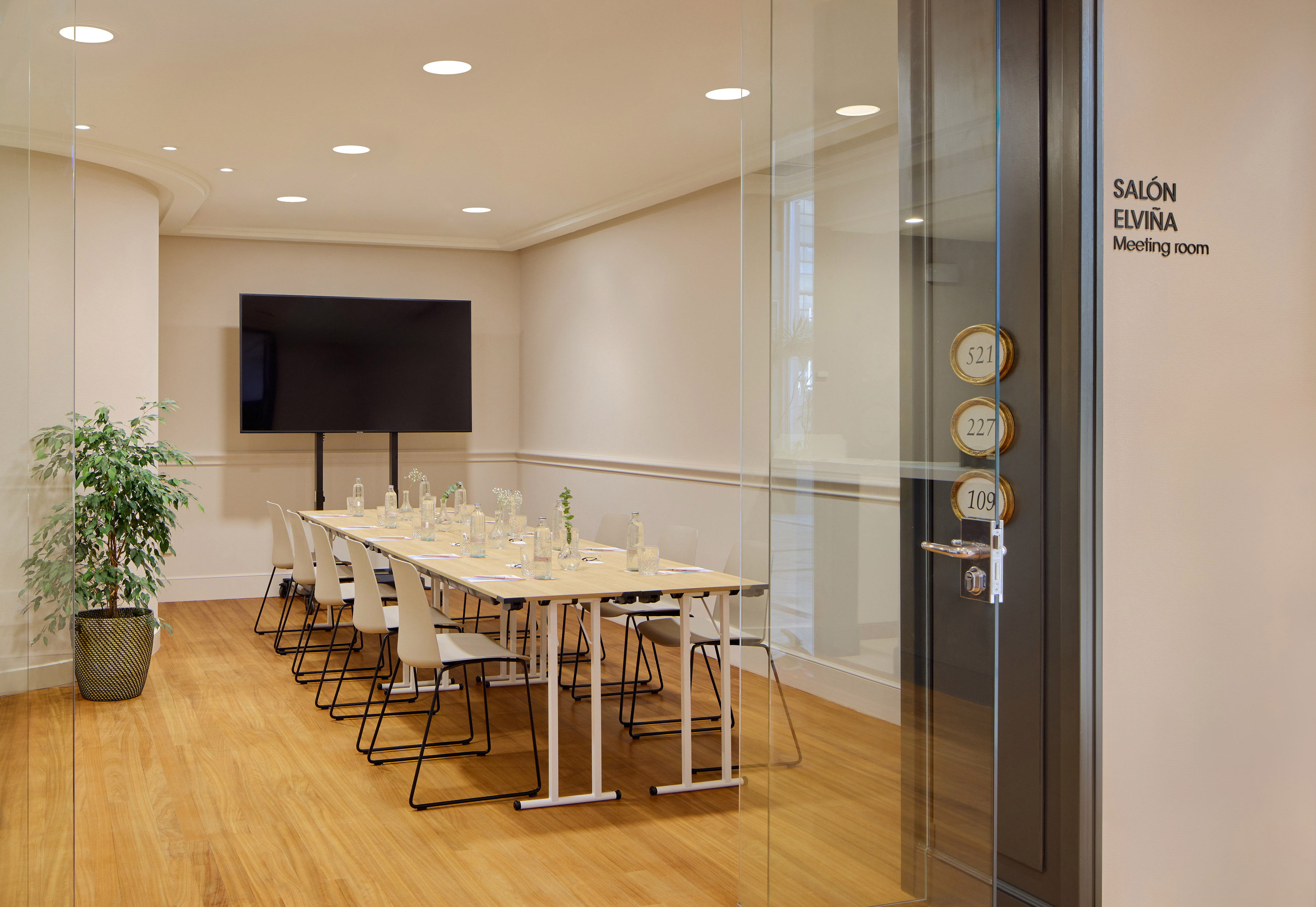 Modern conference room with long table, chairs, large TV, and wooden floor.