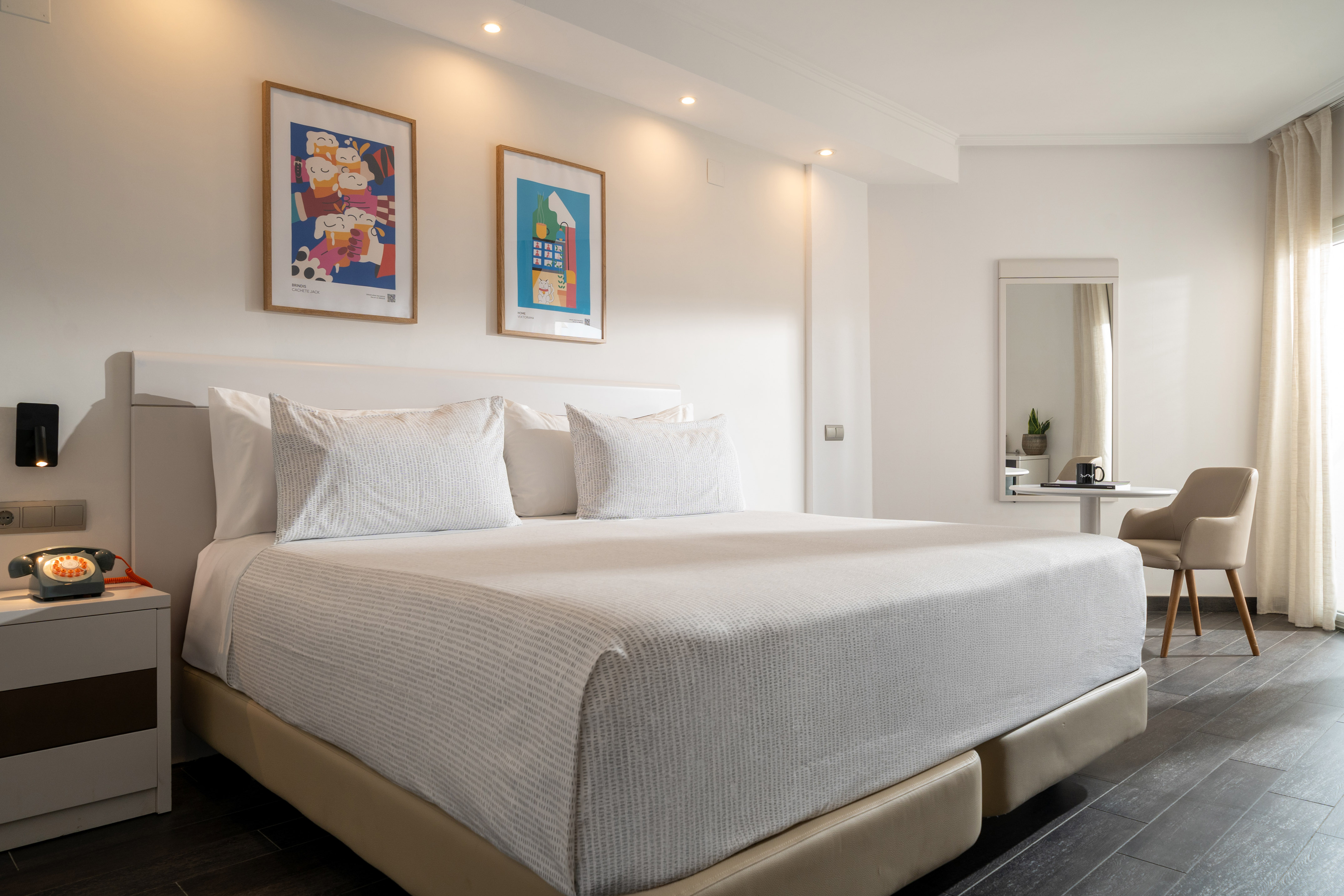 Spacious hotel bedroom with white king bed, modern art, and dark floor.