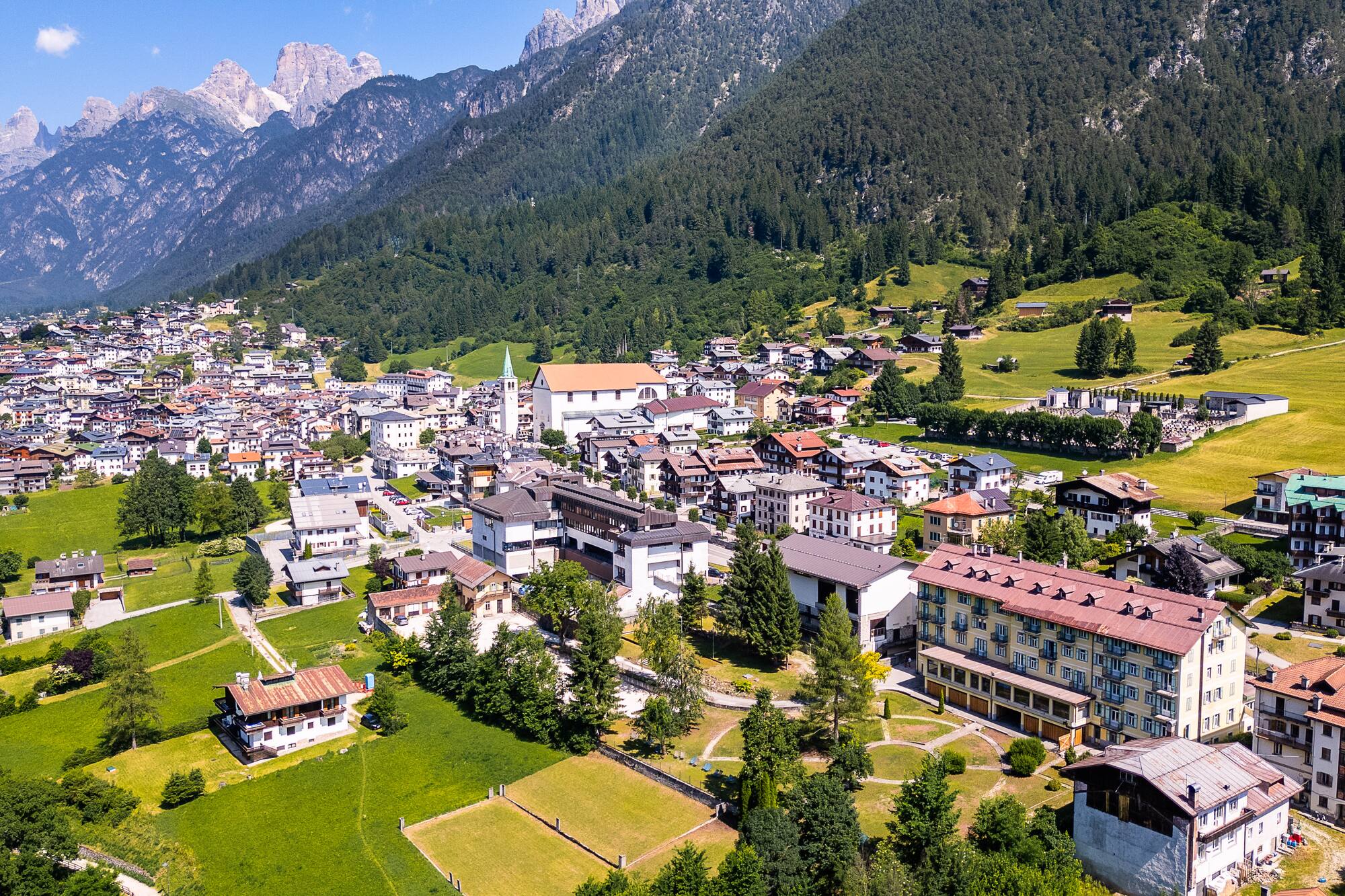 Dolomite village and church nestled among green fields, forests, and mountains.