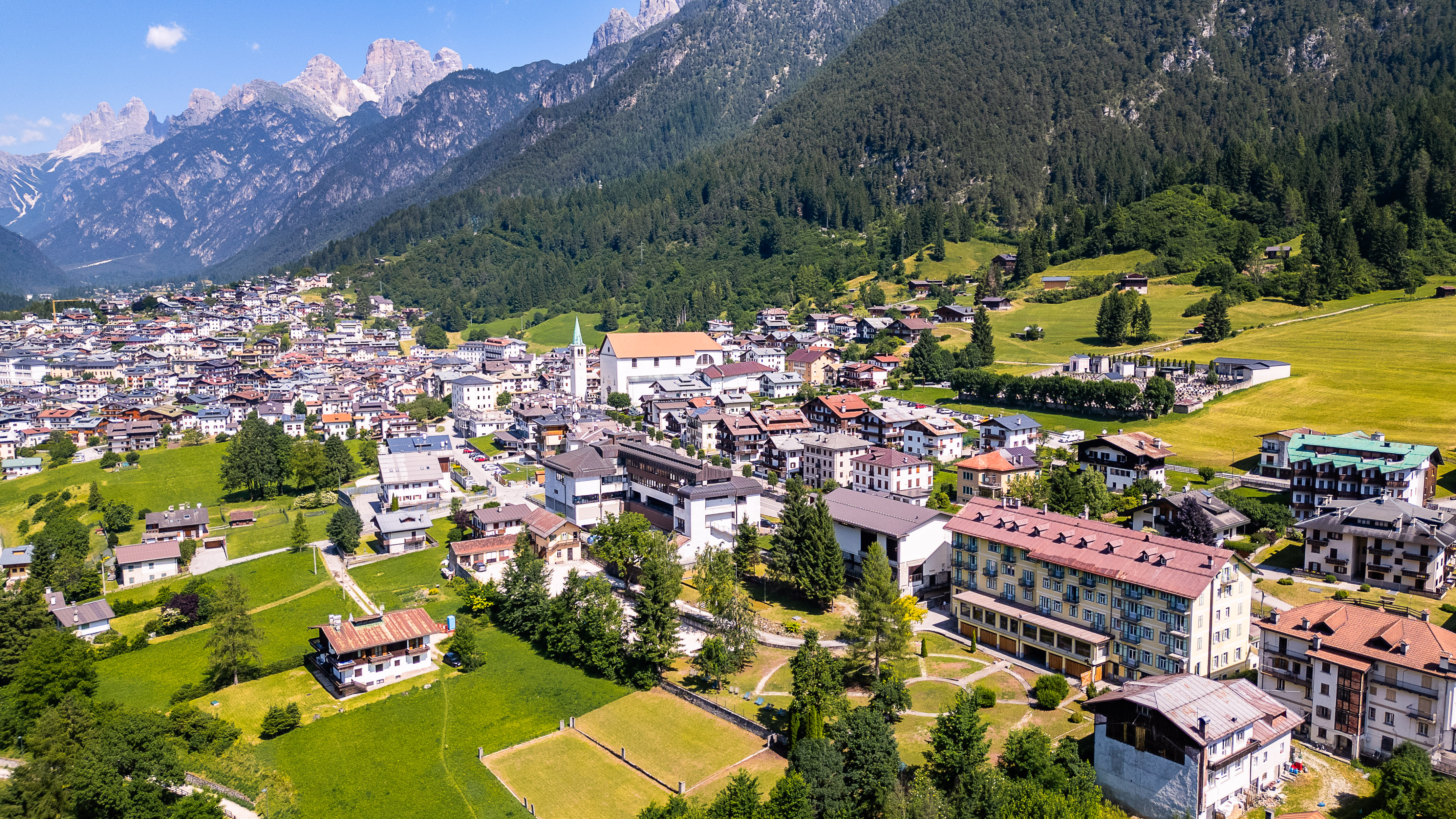 Dolomite village and church nestled among green fields, forests, and mountains.