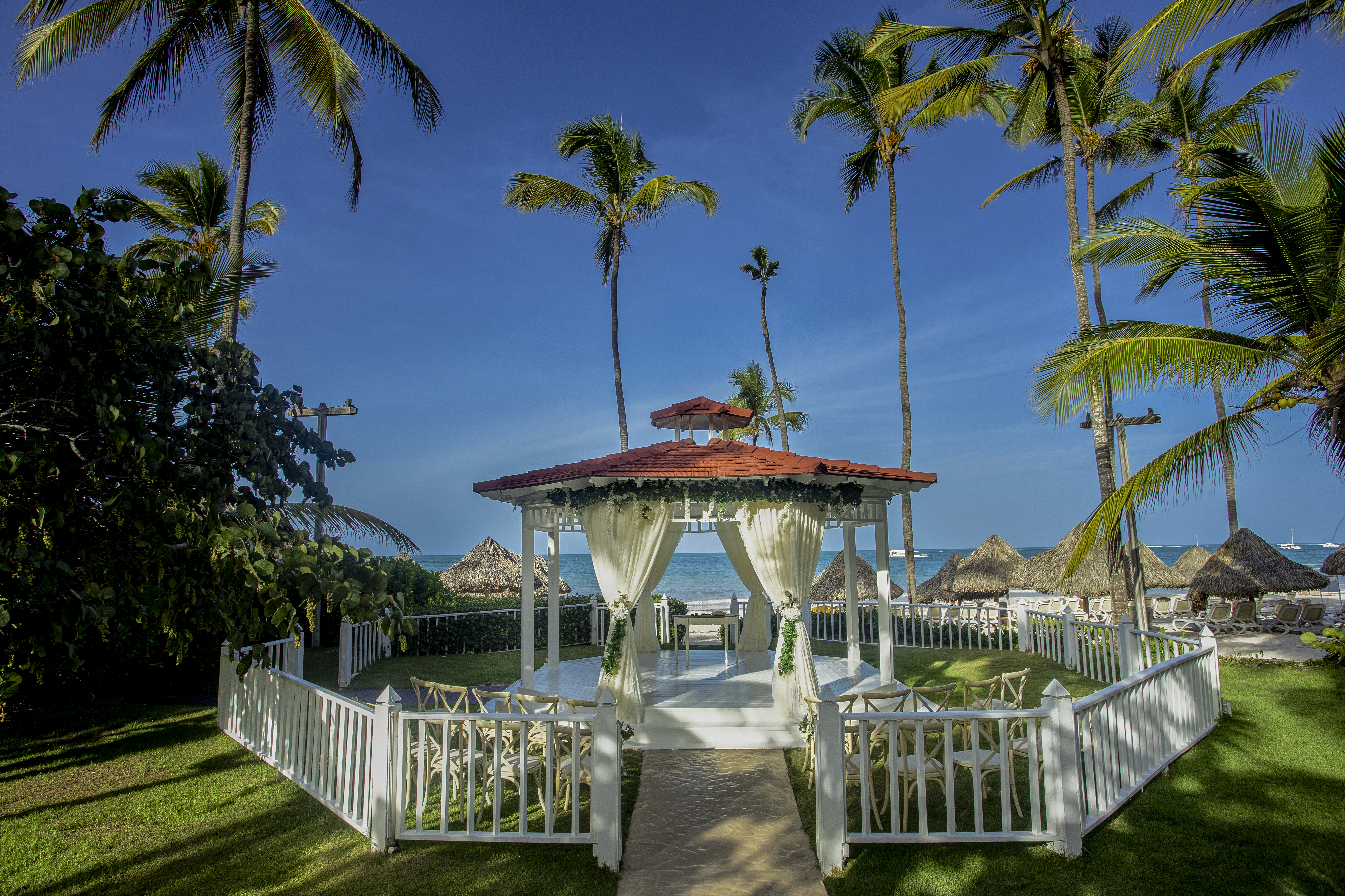 a white gazebo with white curtains and a white fence surrounded by palm trees