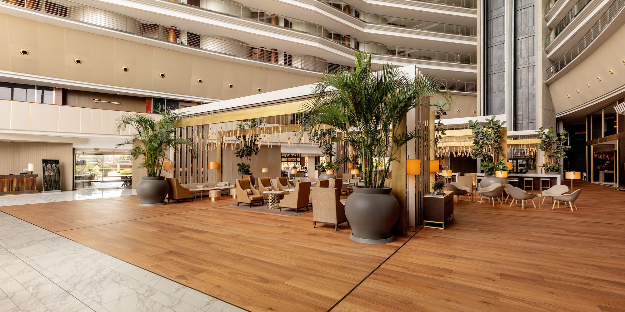 Grand modern hotel lobby with multi-story atrium, lounge seating, and wood floors.