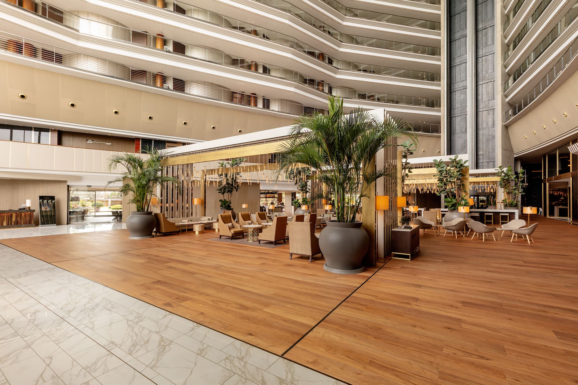 Grand modern hotel lobby with multi-story atrium, lounge seating, and wood floors.