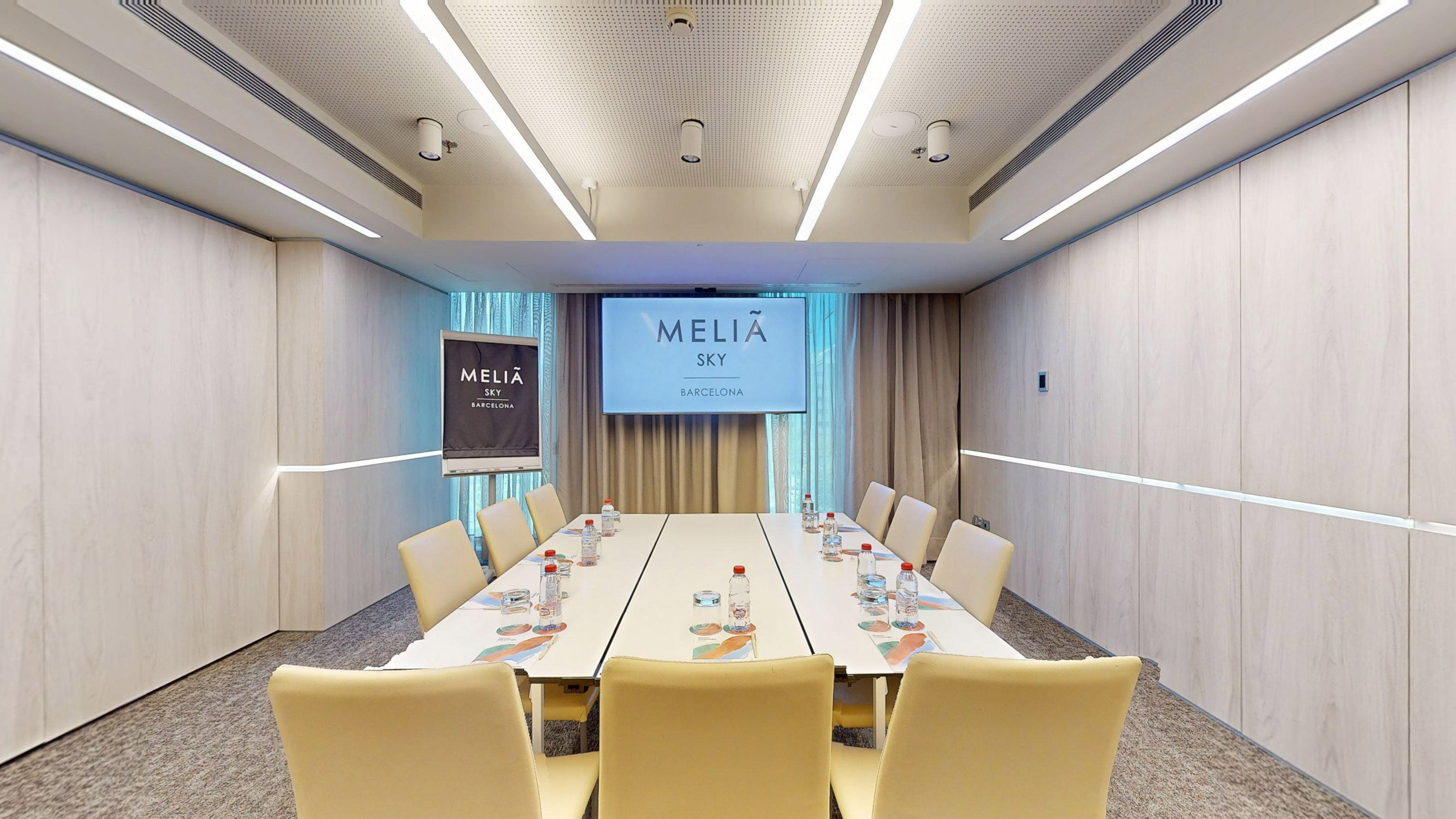 Modern Melia Sky Barcelona meeting room with conference table and display screen.