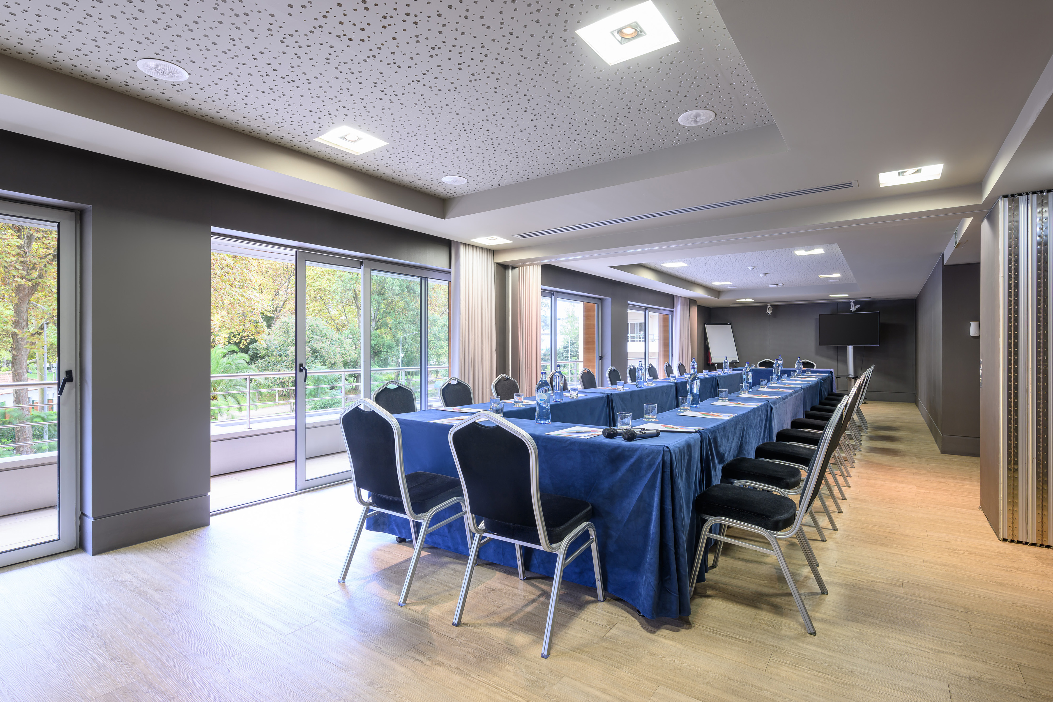 Meeting room with blue table setup, chairs, large windows, and garden view.