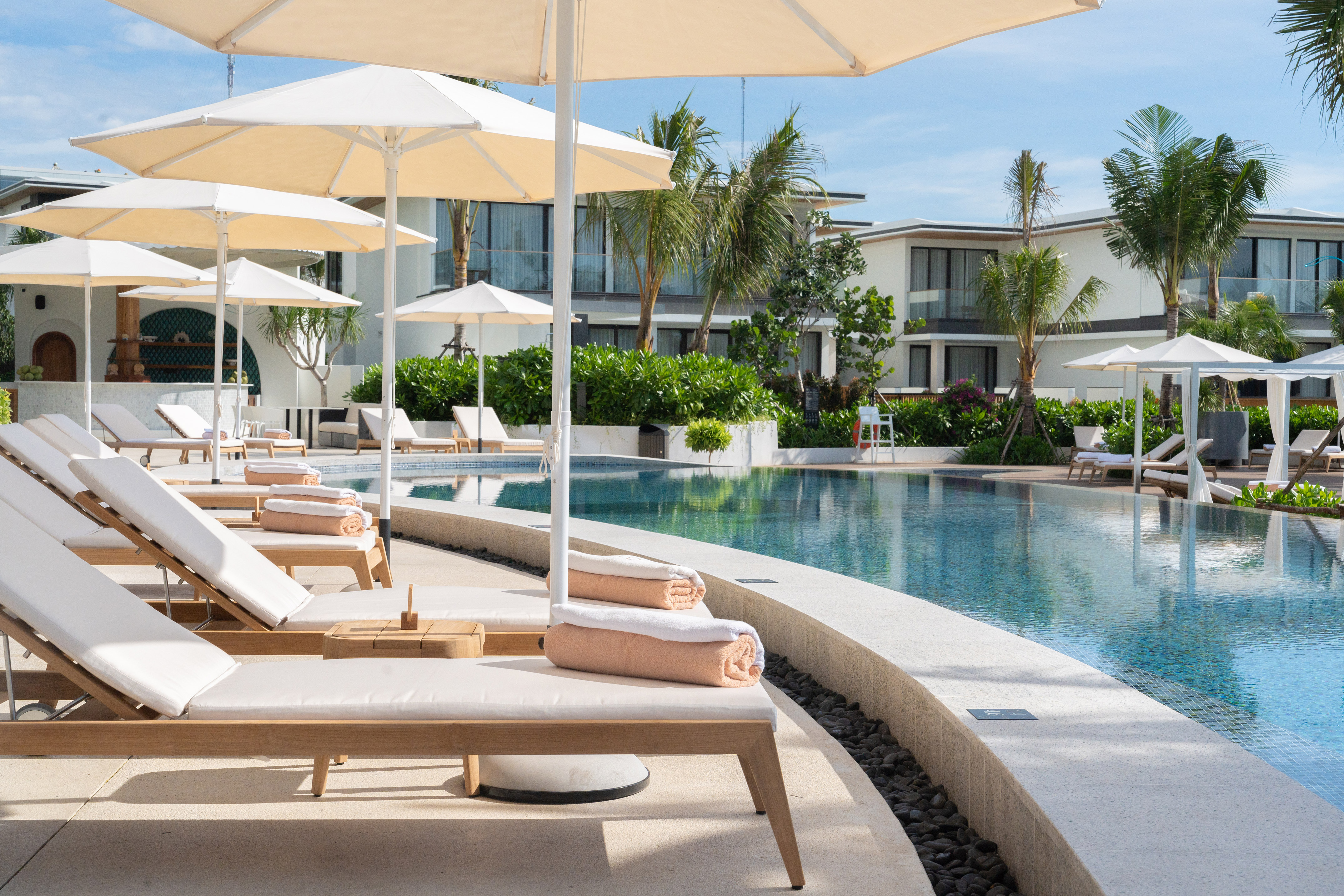 Luxury resort swimming pool with sun loungers, umbrellas, and tropical plants.